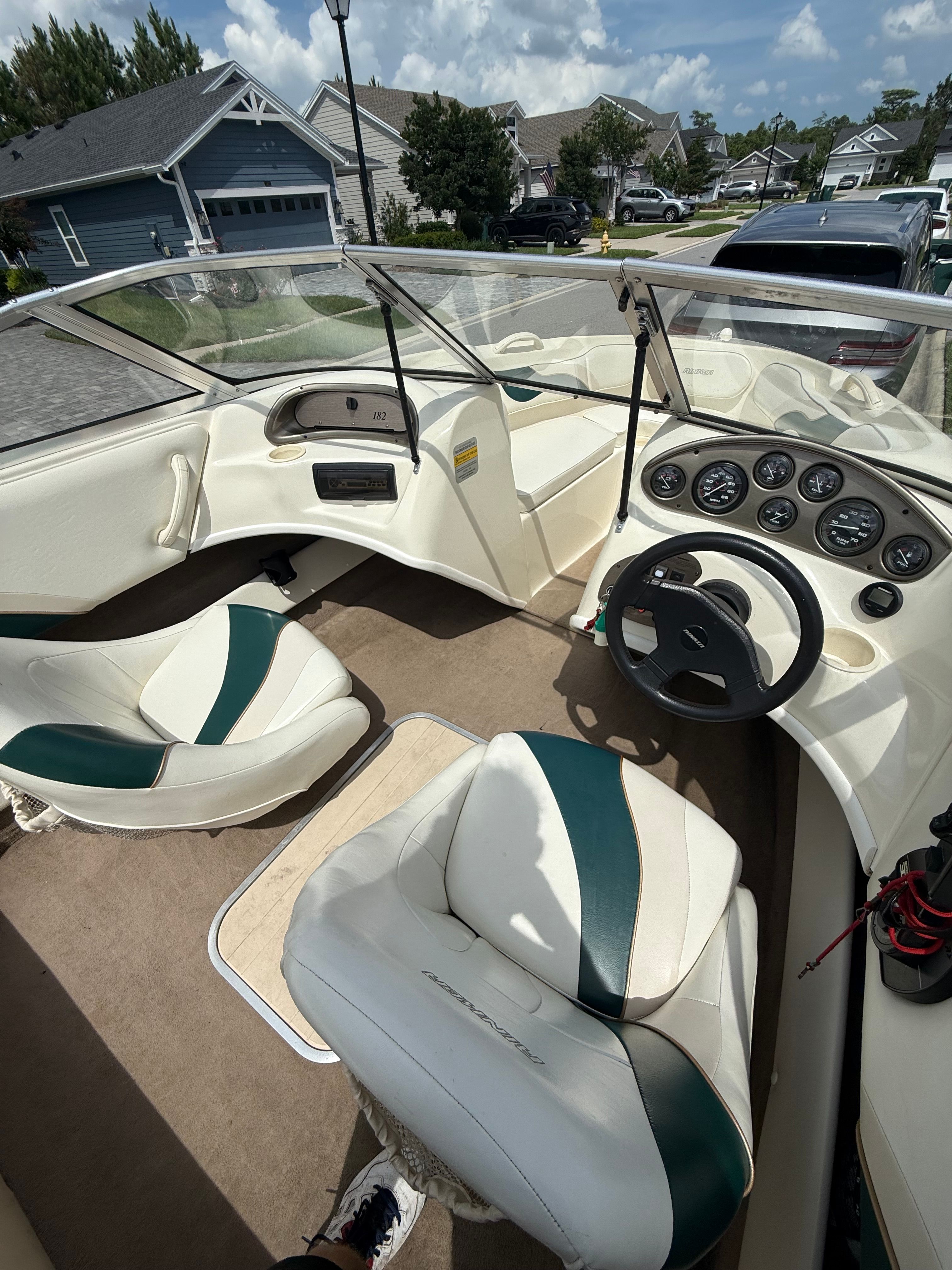 Interior view of a boat with white seats and dashboard, parked in a residential area.
