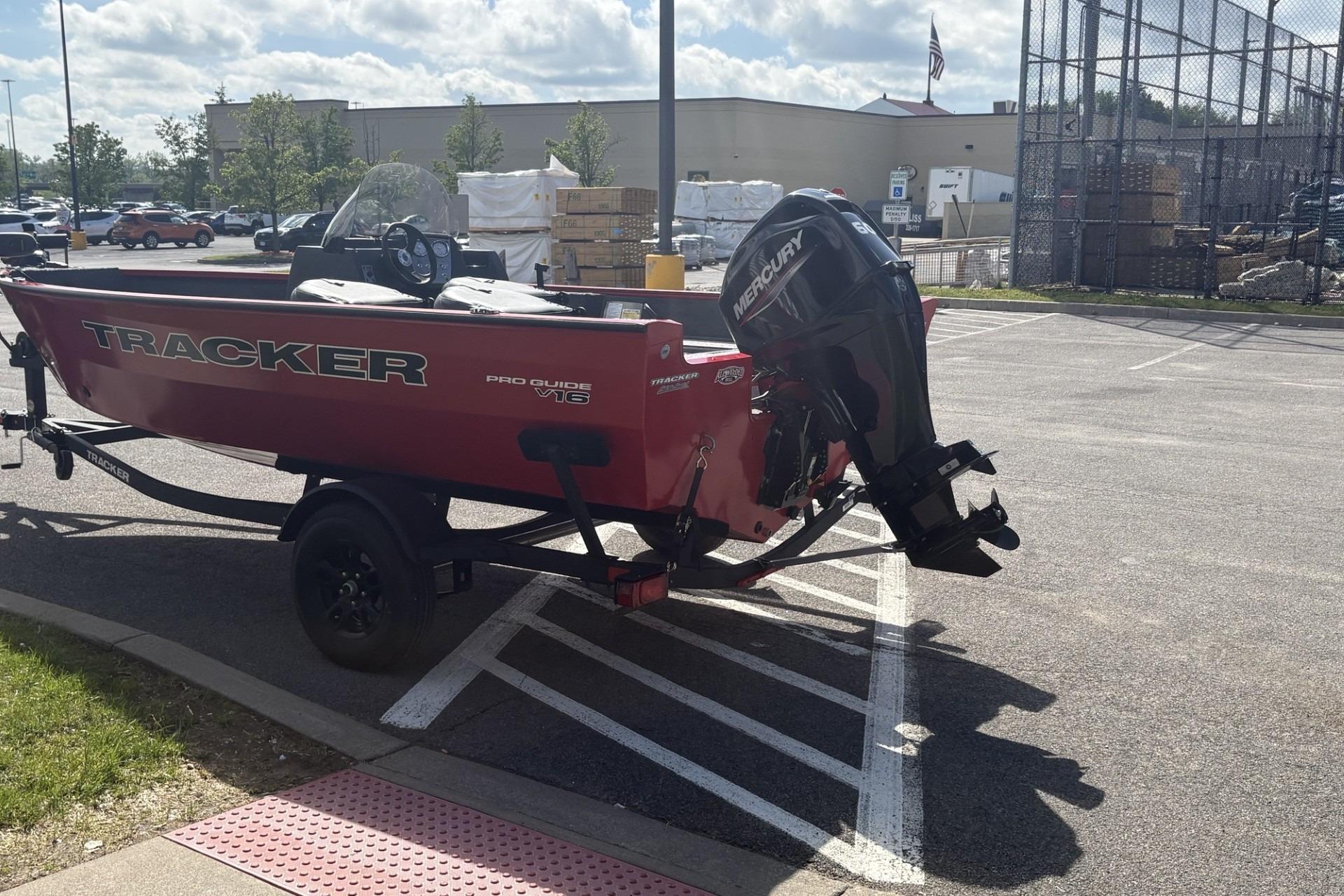 Red 2026 Tracker Pro Guide V-16 SC boat with Mercury engine in parking lot.