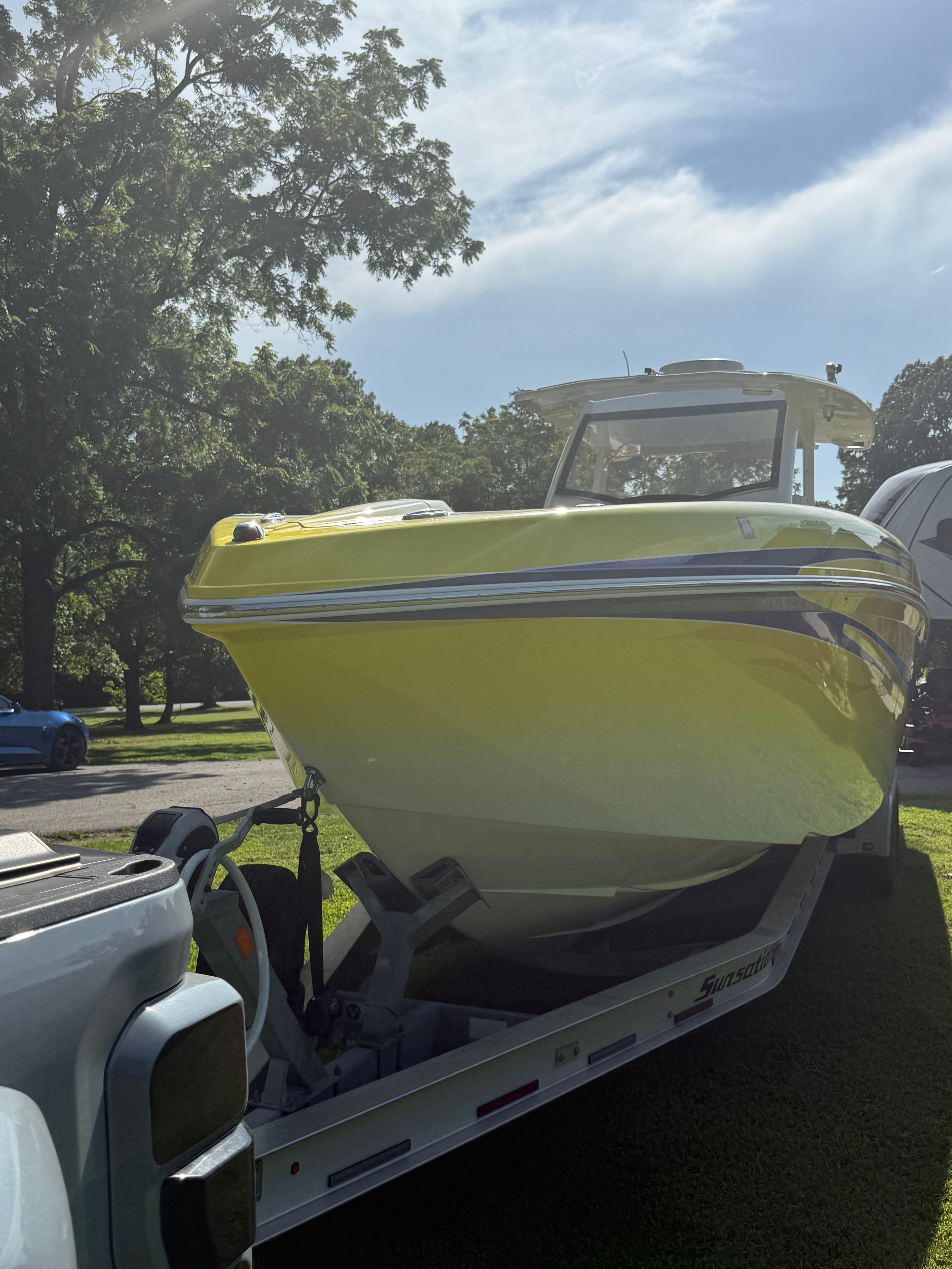 A yellow boat on a trailer, surrounded by trees and a blue sky.