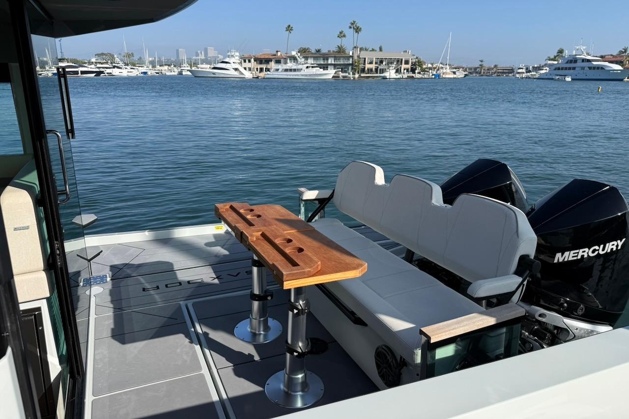 2024 Saxdor 320 GTC boat interior with seating, table, and Mercury engines on a sunny day.