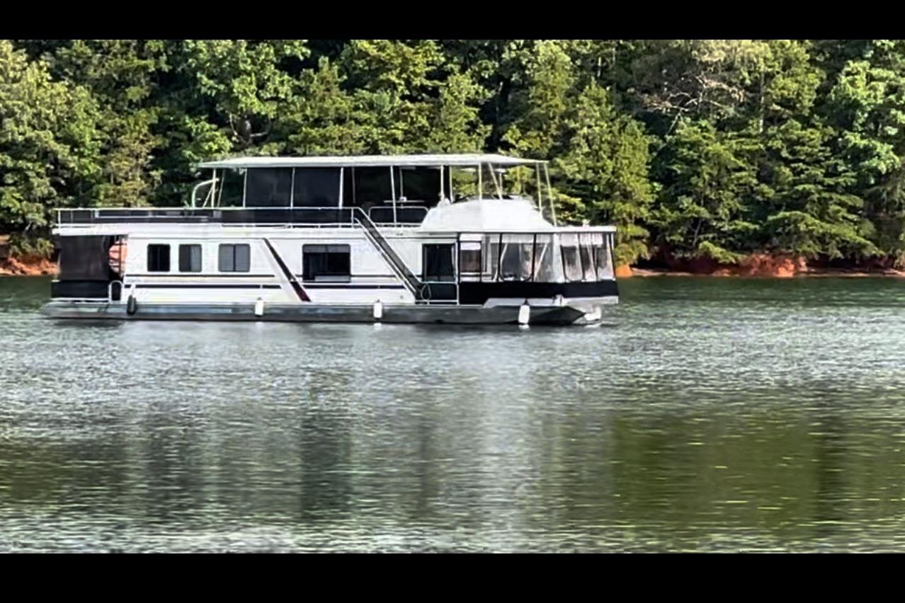 Houseboat on a serene lake, surrounded by lush green trees, Sumerset 66, 1992 model.