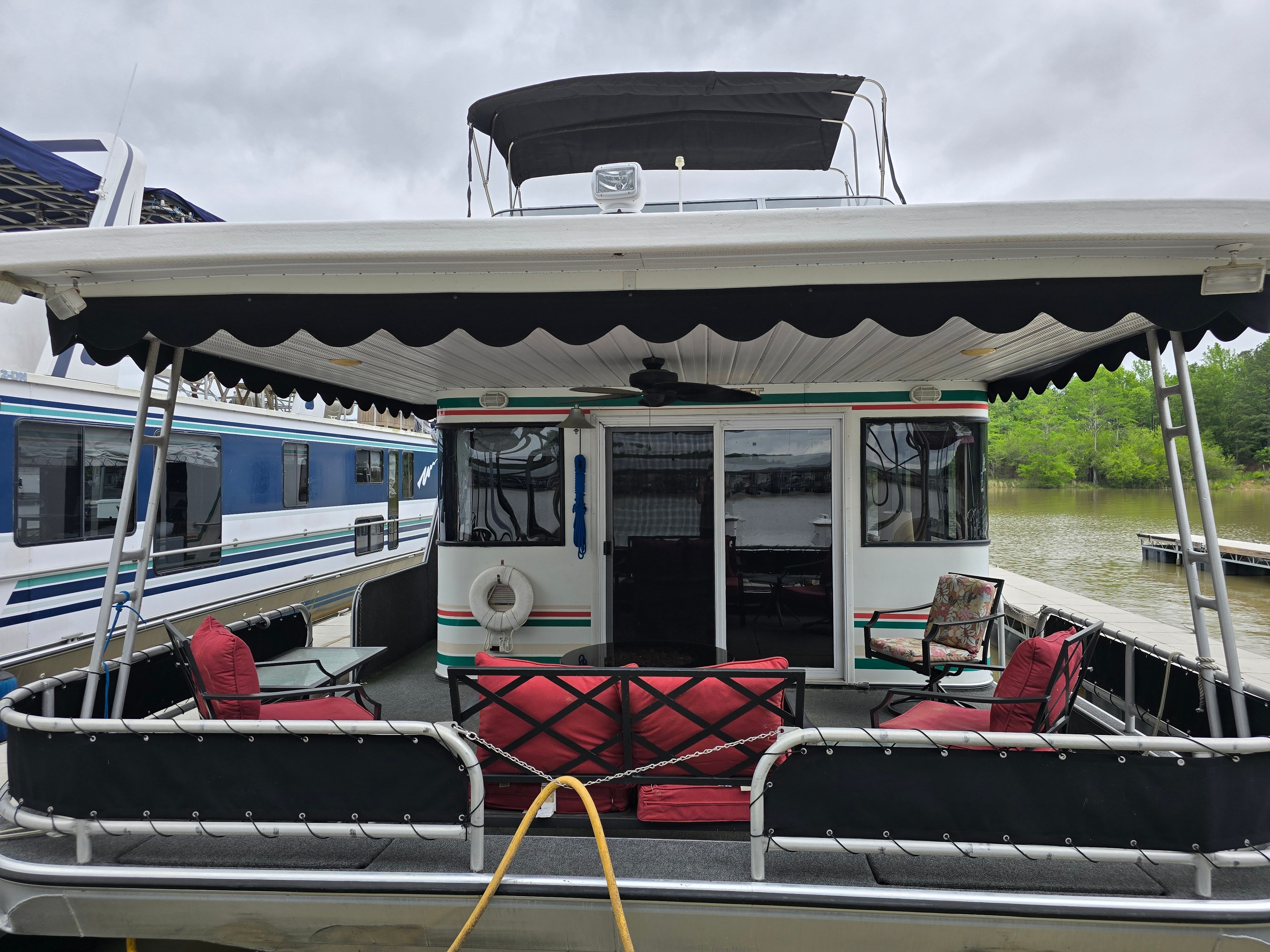 1998 Sumerset houseboat with outdoor seating, docked on a calm lake under cloudy skies.