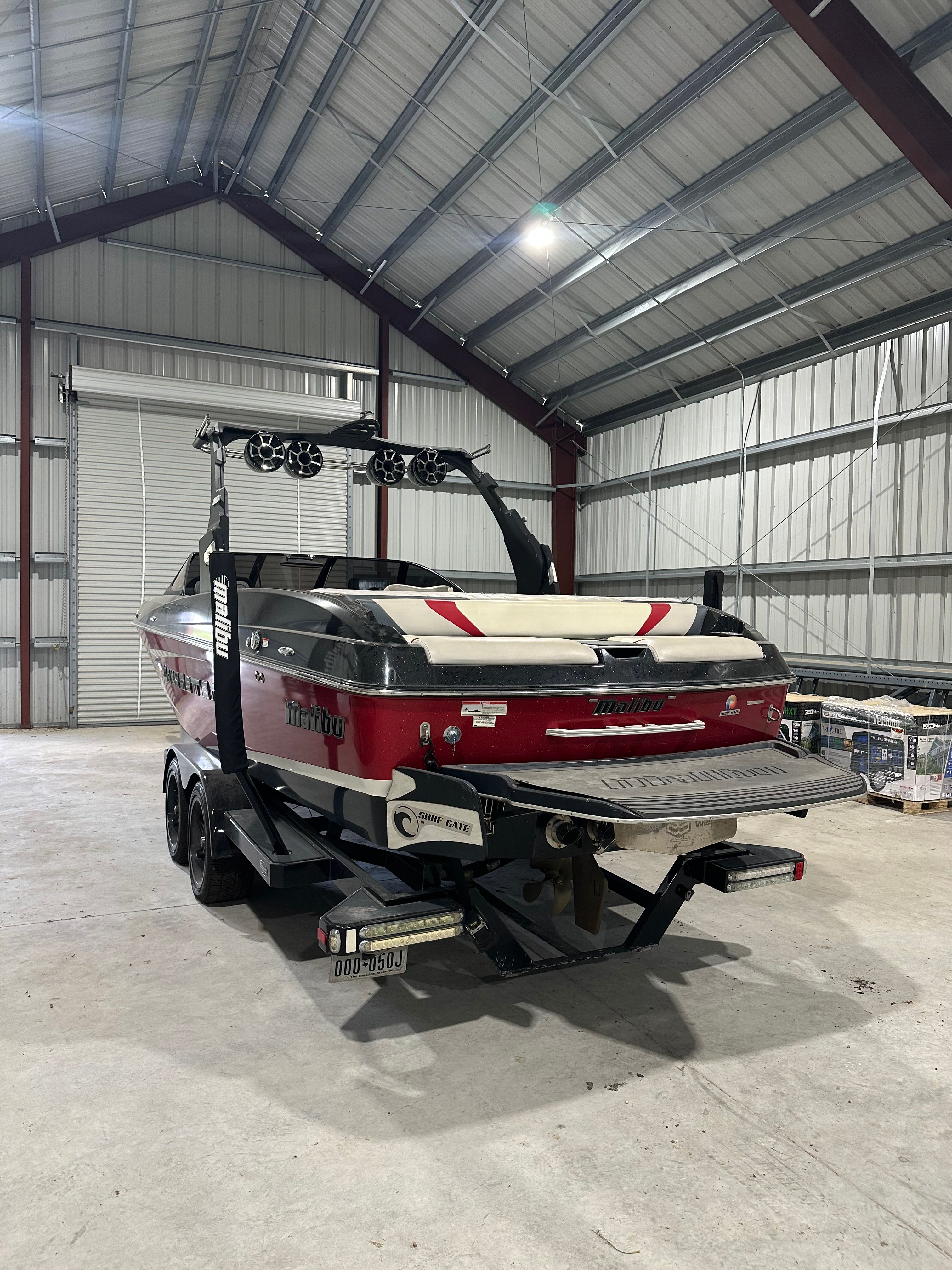 A red Malibu Wakesetter 24 MXZ boat is parked in a warehouse.