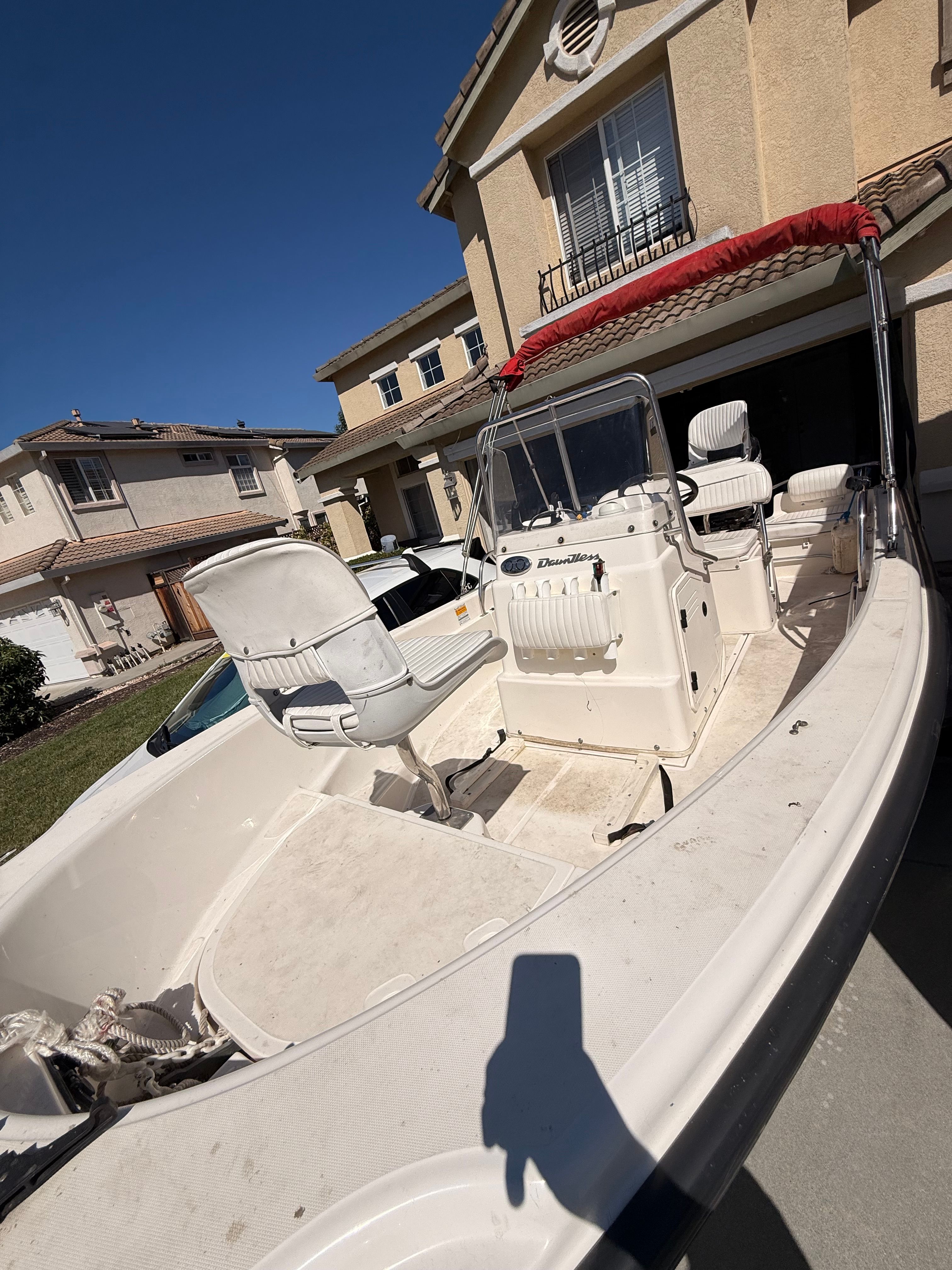 A 2002 Boston Whaler 160 Dauntless in a driveway. It features white seats and a red canopy.
