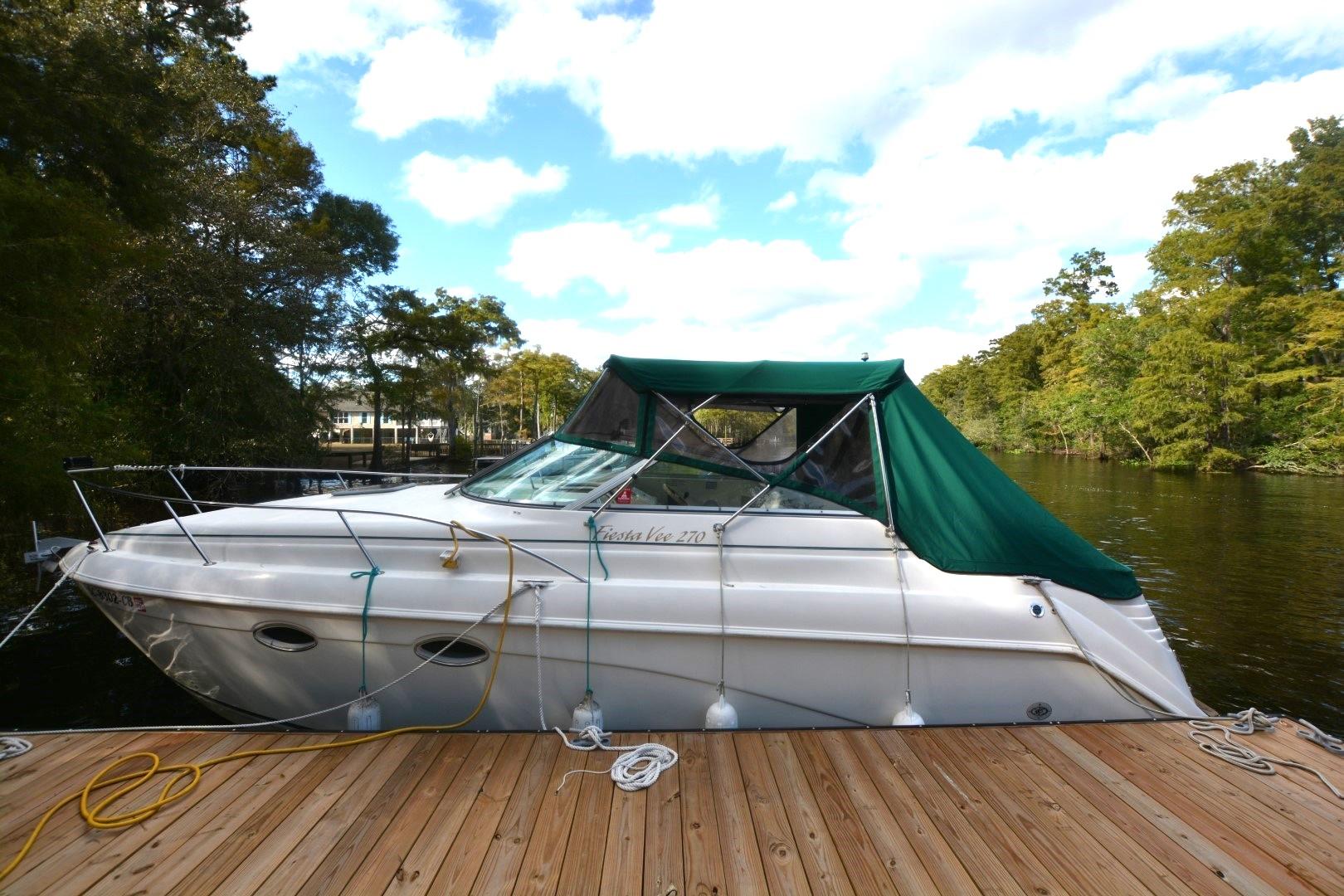 1999 Rinker 270 Fiesta Vee boat docked on a serene lake with green canopy.