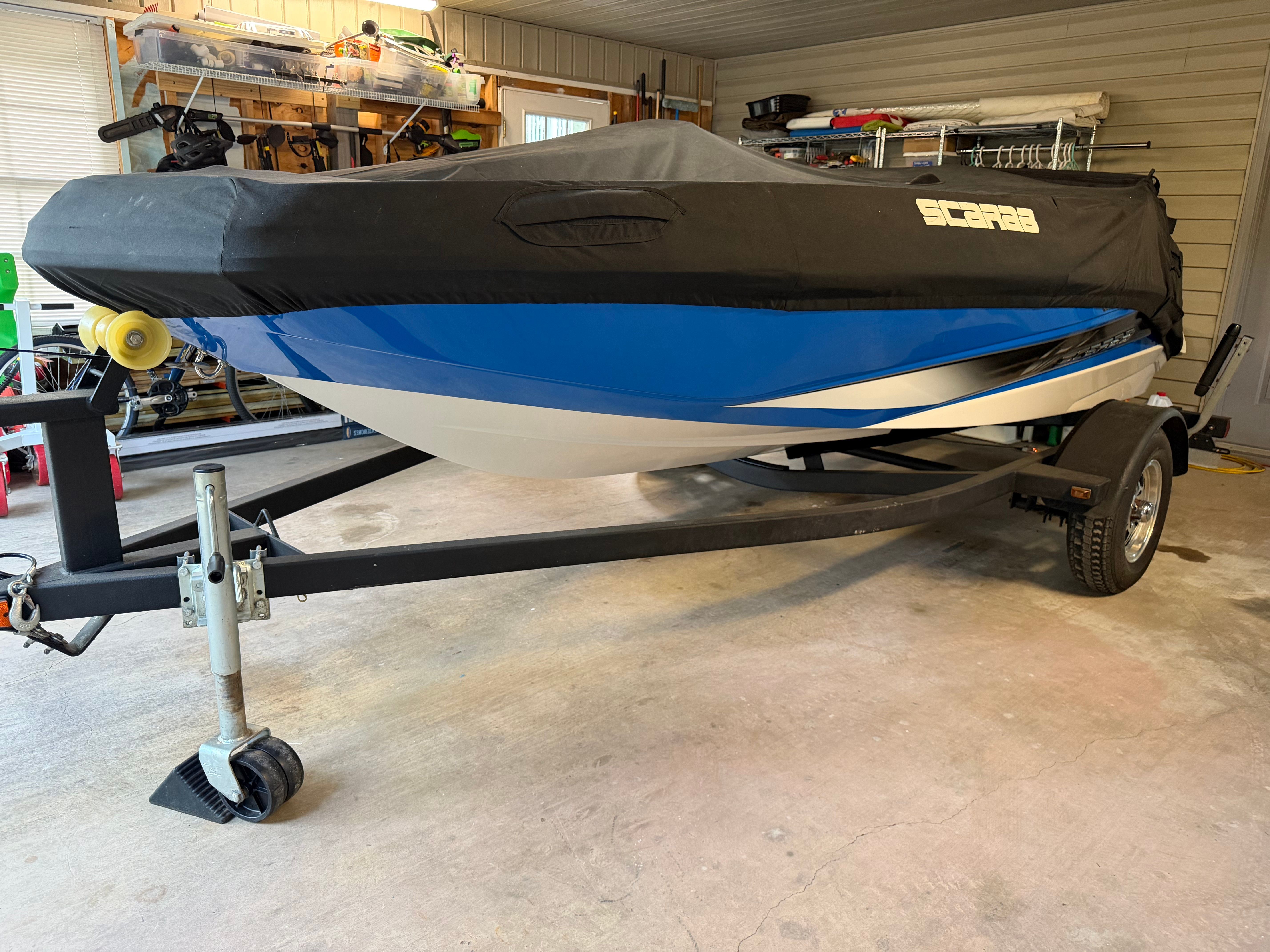A 2015 Scarab 165 boat with blue and white paint, covered and on a trailer.
