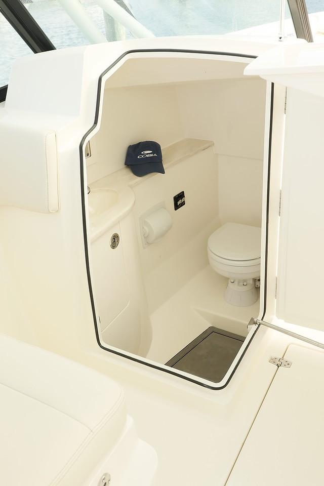 2024 Cobia 280 Dual Console boat interior bathroom with toilet and storage shelf.