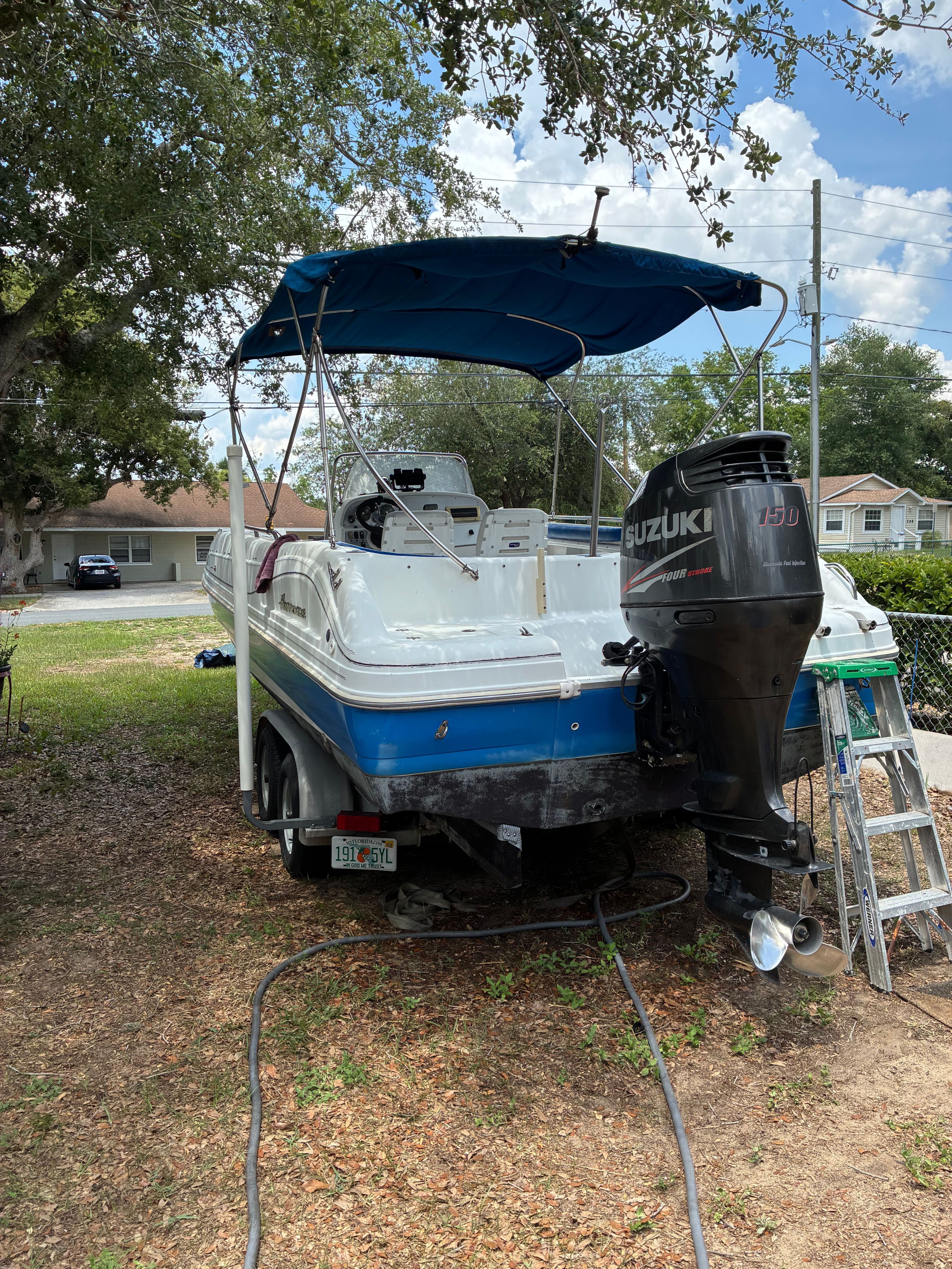 A blue and white boat with a Suzuki outboard motor sits on a trailer in a yard.