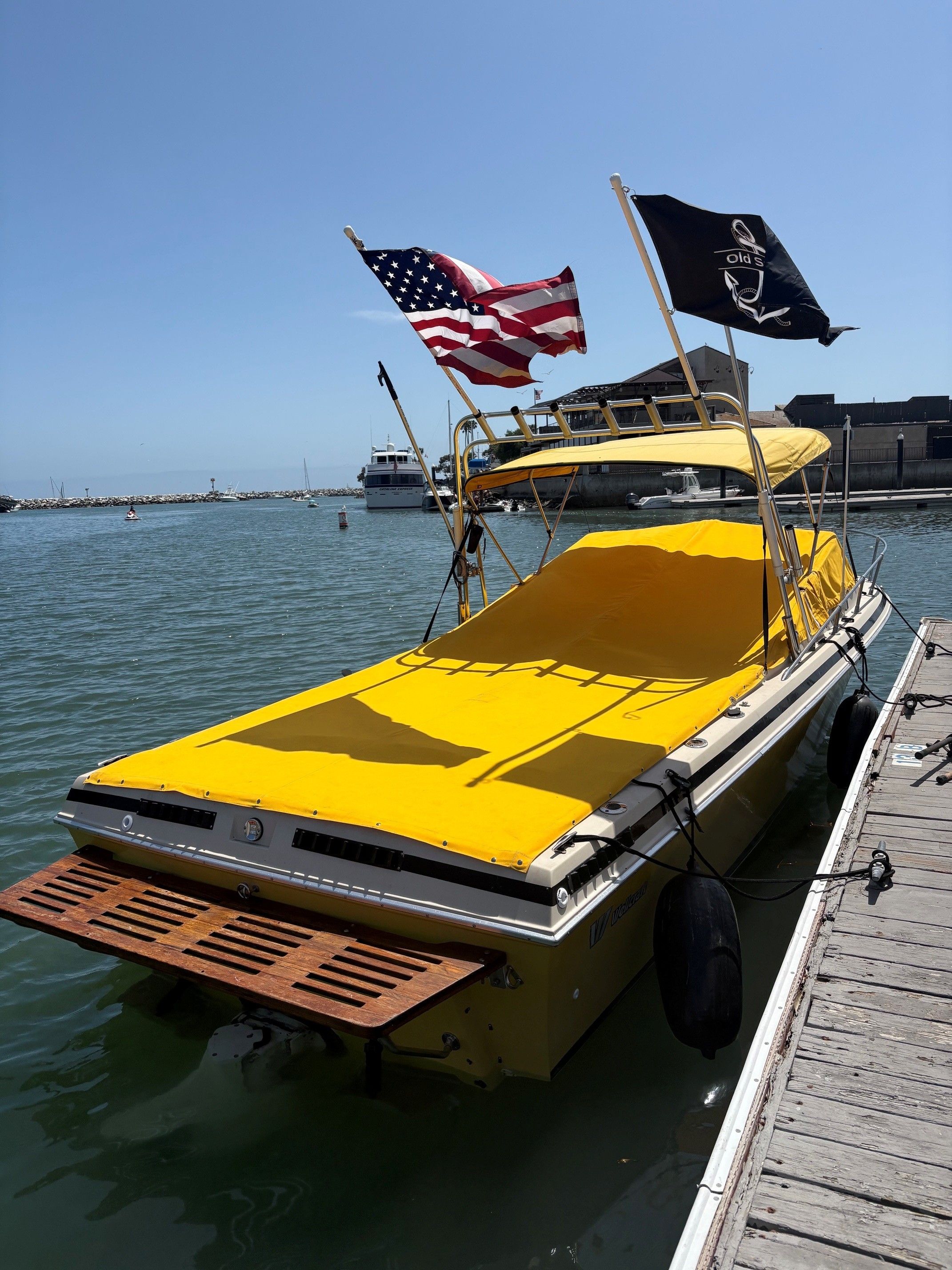 1979 Wellcraft Nova 250 boat with yellow cover and flags in harbor.