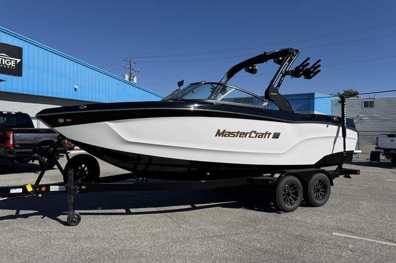 2026 MasterCraft XT22 boat on trailer, parked outdoors near blue building.