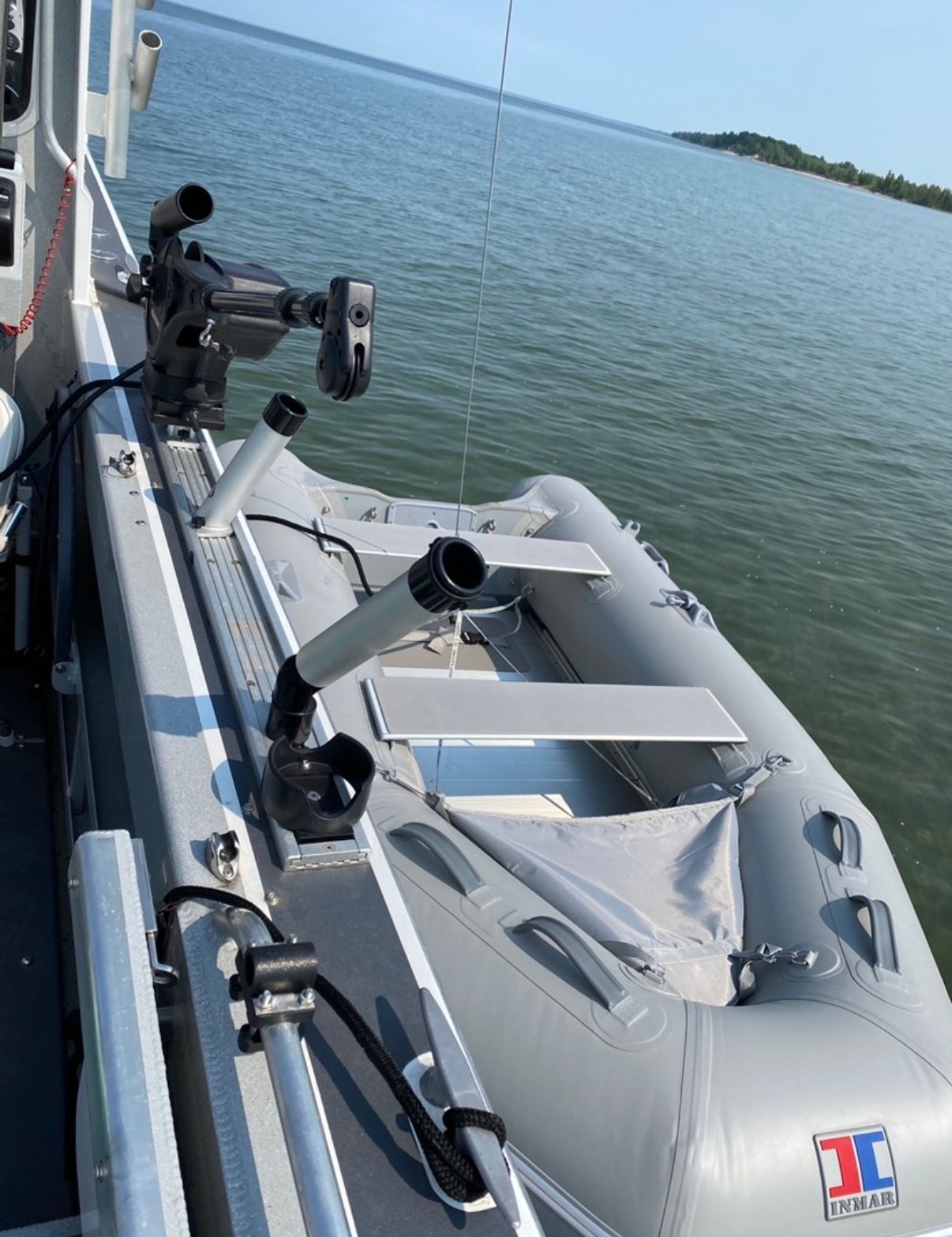 An inflatable boat on a larger boat, with fishing rod holders and calm water in the background.