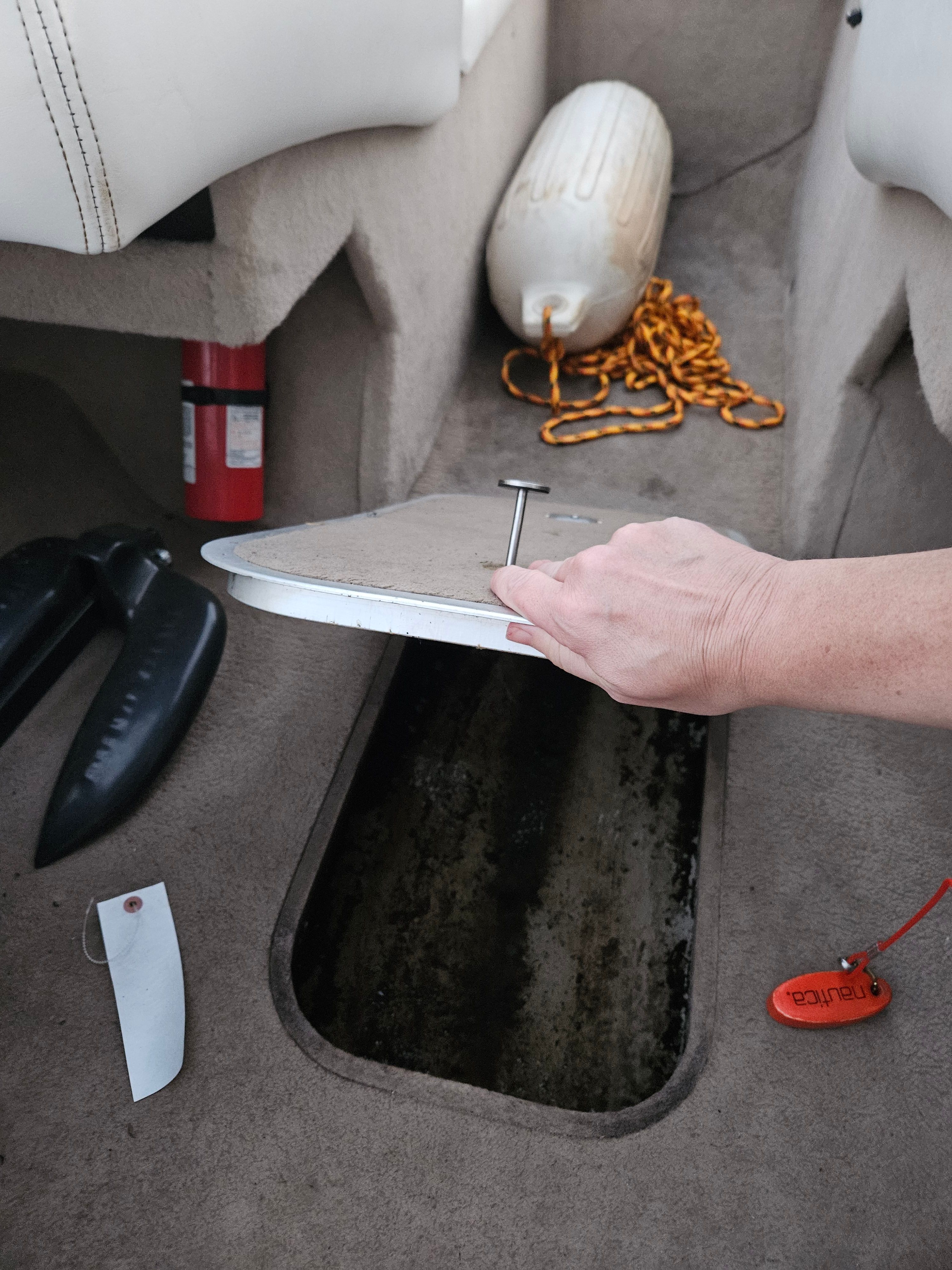 A person opens a floor hatch in a boat, surrounded by safety equipment.