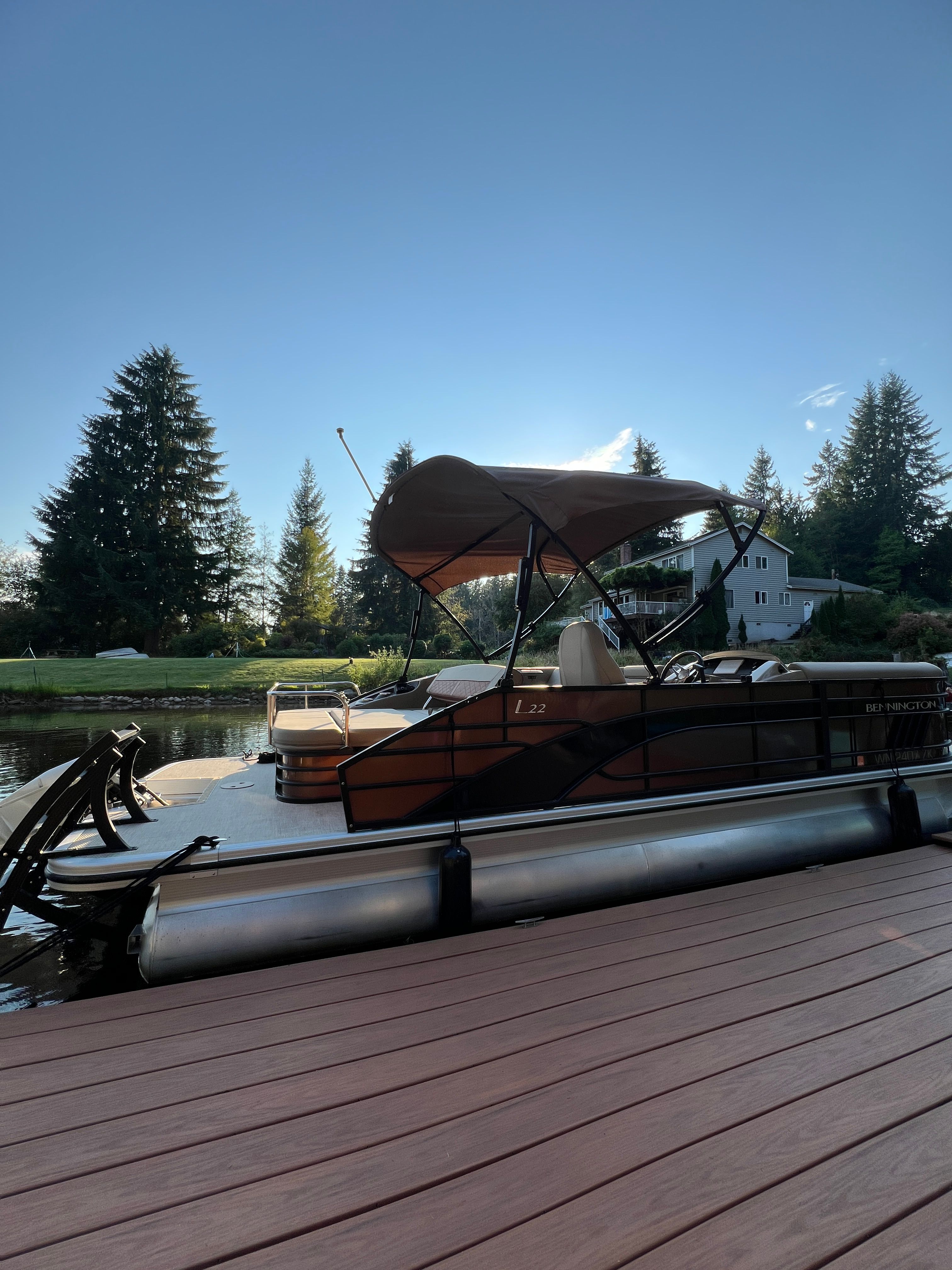 A Bennington 22 LSB pontoon boat is docked at a wooden pier. It features a sunshade and is surrounded by trees.