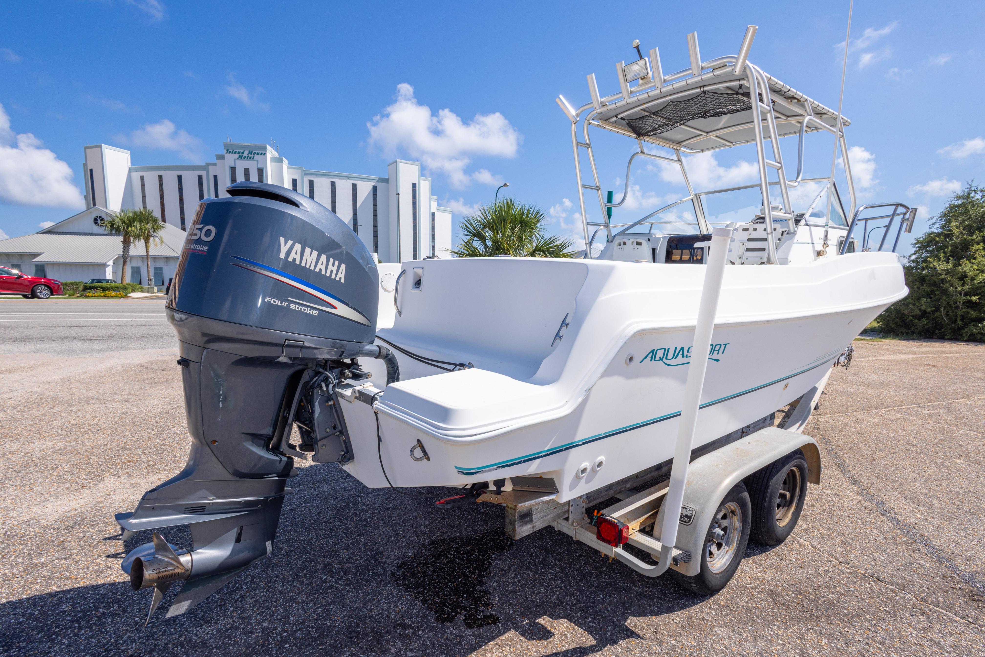1999 Aquasport 225 Explorer boat with Yamaha engine on trailer, parked outdoors.