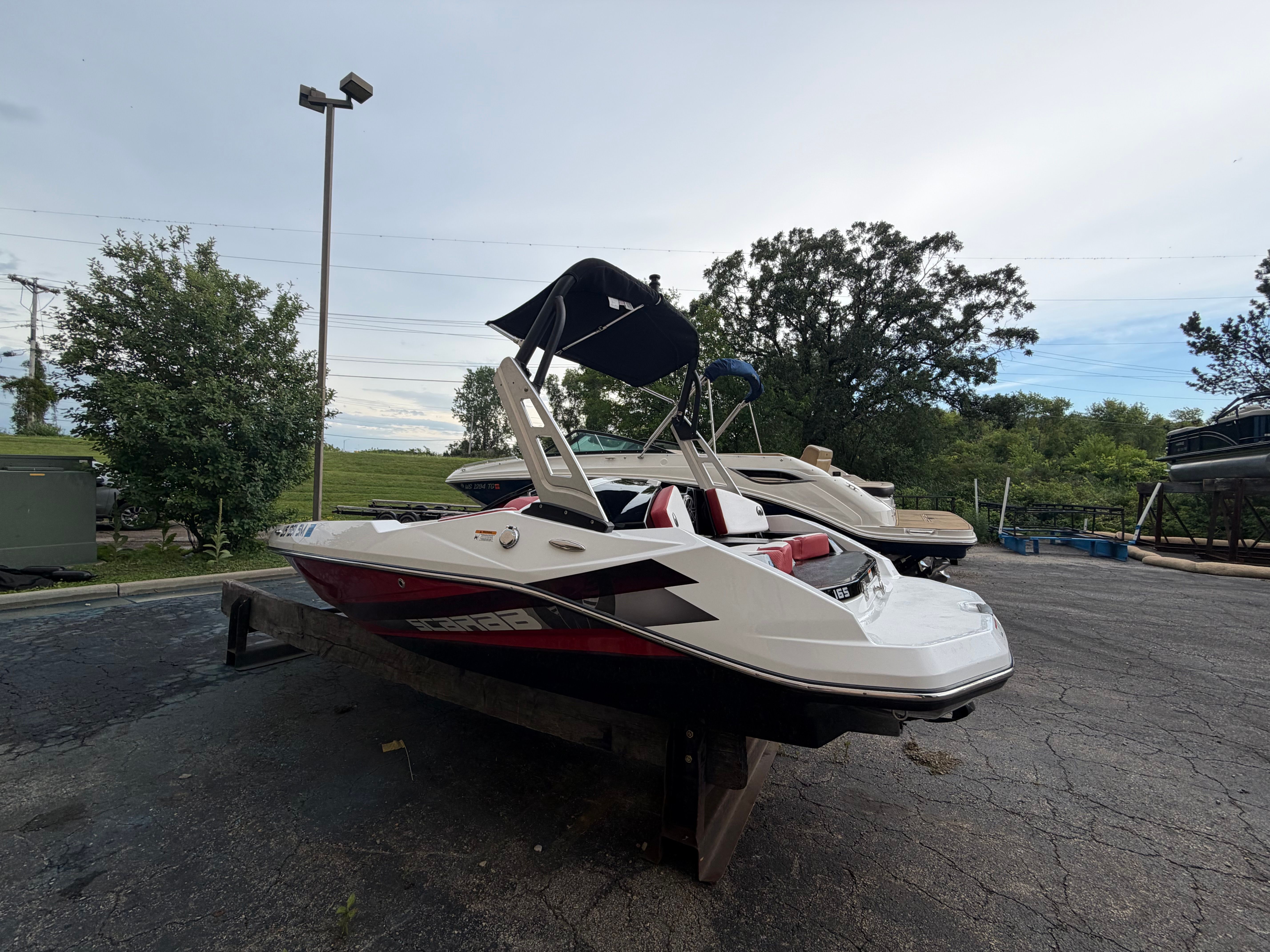 A 2021 Scarab 165 ID boat on a trailer, surrounded by trees and another boat.