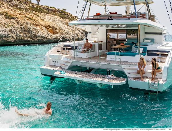 2025 Lagoon 55 yacht in turquoise waters, people relaxing and swimming nearby.