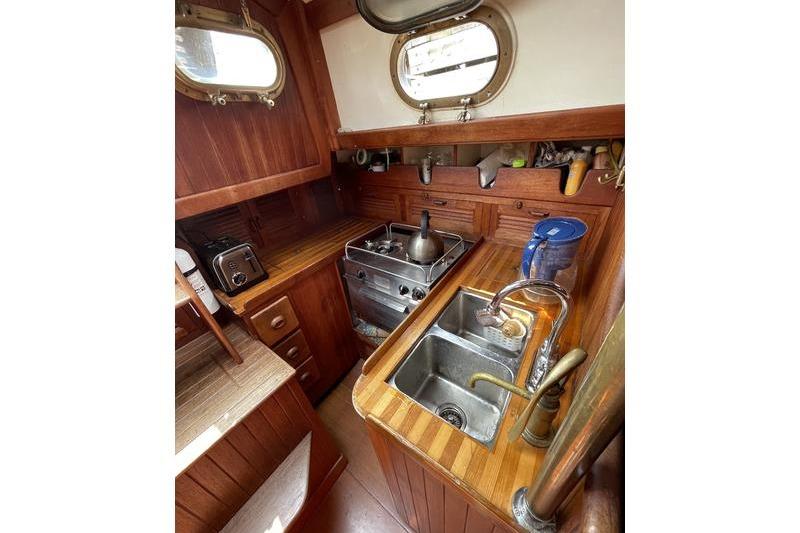 Compact galley kitchen in 1980 Ta Shing Baba 30 sailboat with wooden cabinetry and stainless steel sink.