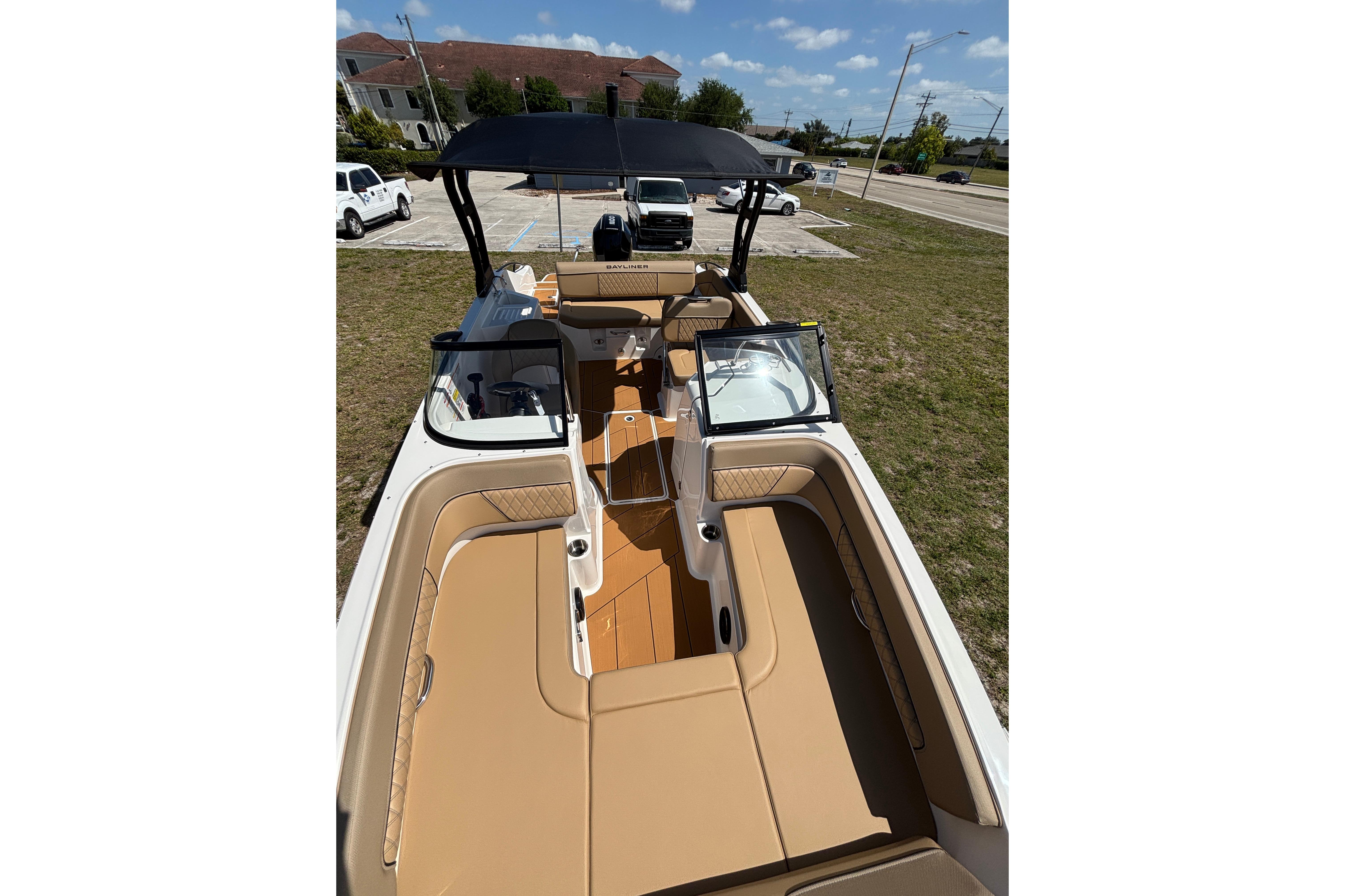 2026 Bayliner D22 boat with tan seating and black canopy, parked on grass.