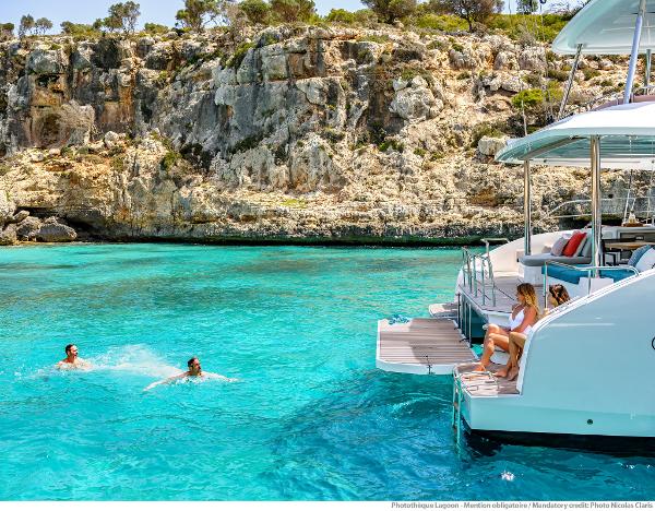 Lagoon 55 yacht in turquoise waters near rocky cliffs, 2025 model.