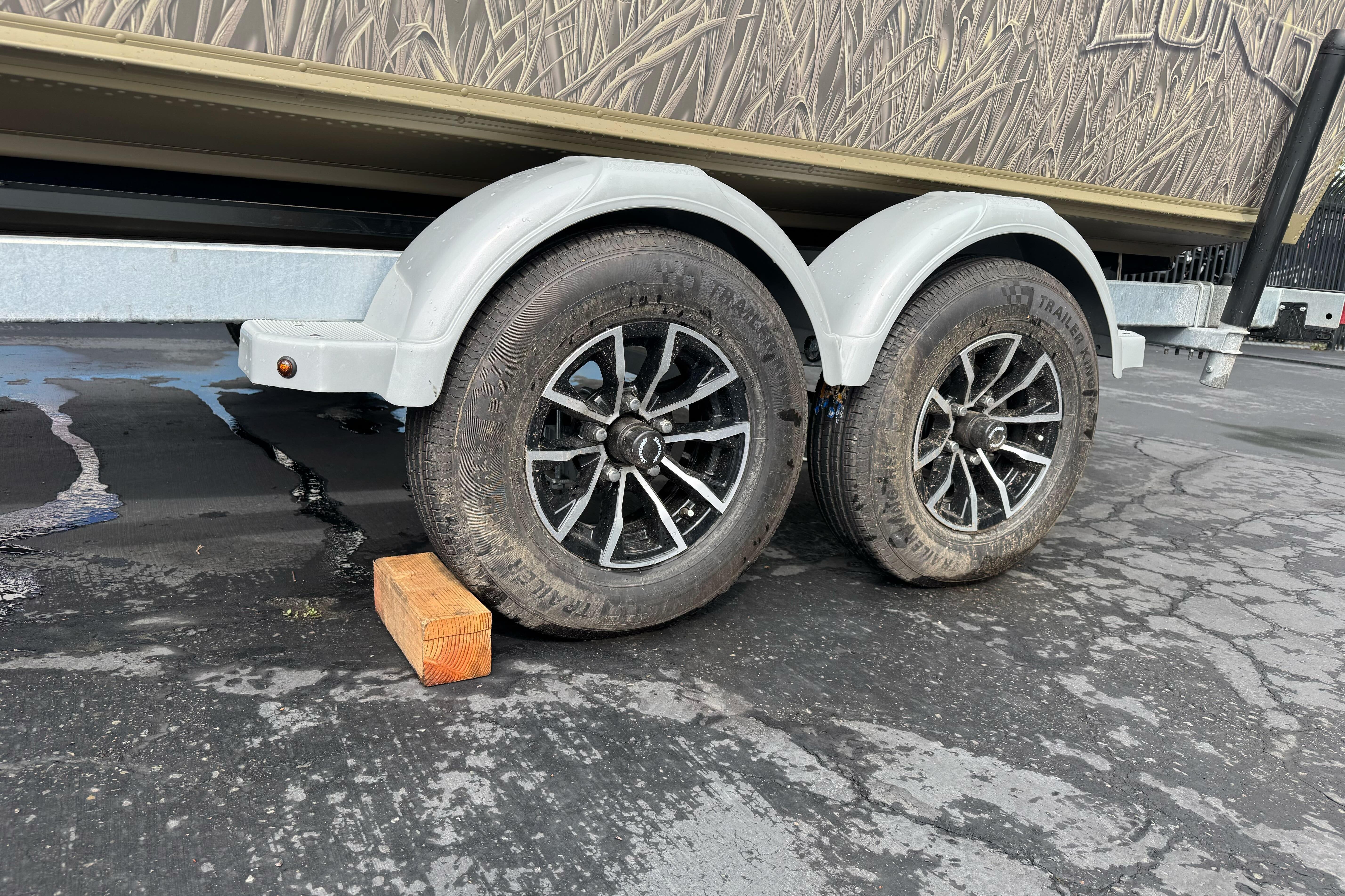 Trailer wheels of 2026 Lund 2075 Alaskan SS, parked on asphalt with wooden block.