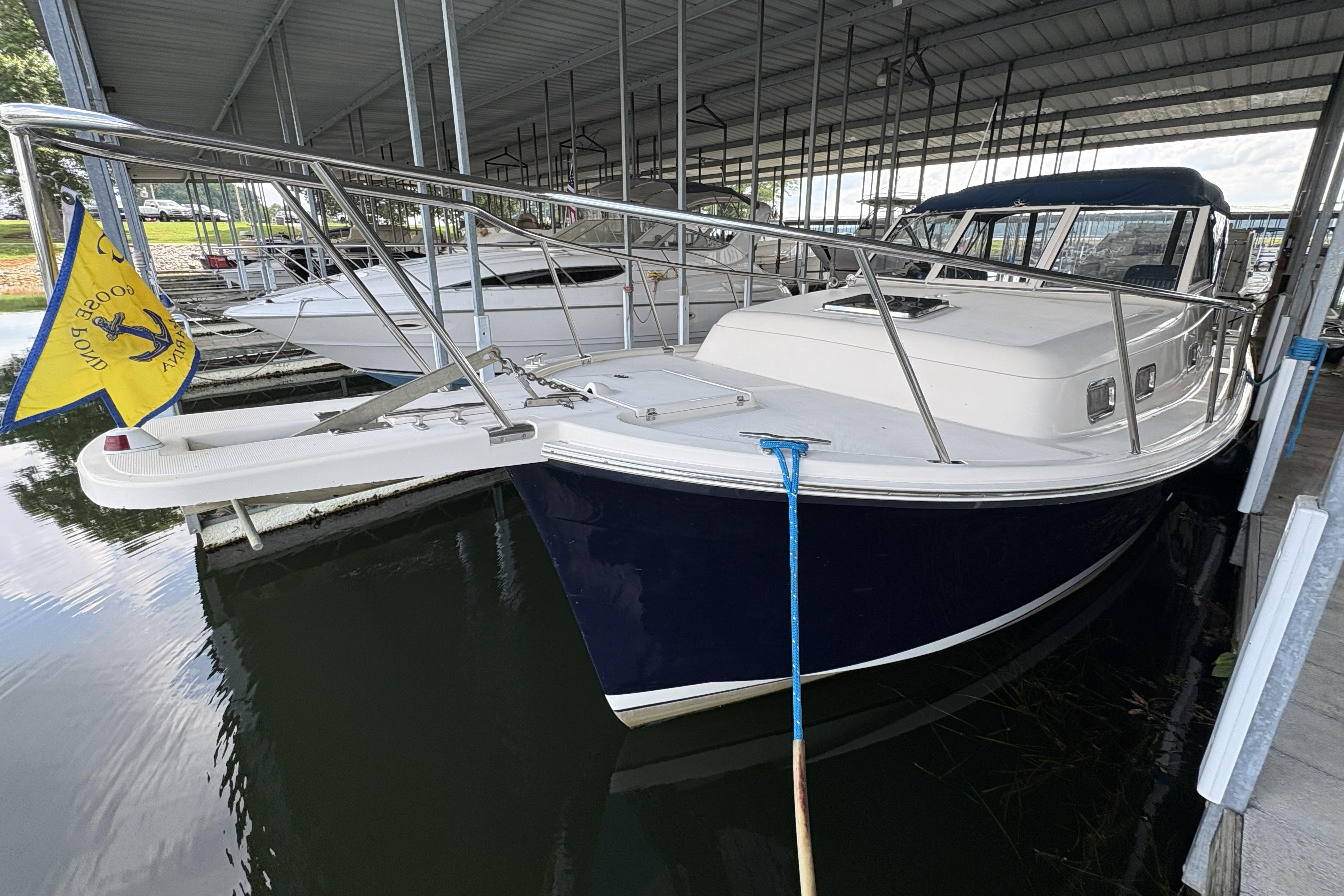 2003 Mainship Pilot 30-II docked under a covered marina, featuring a sleek navy hull.