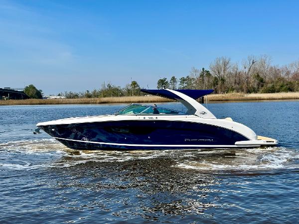 A 2018 Regal 3300 boat cruising on calm water with a wooded shoreline in the background.