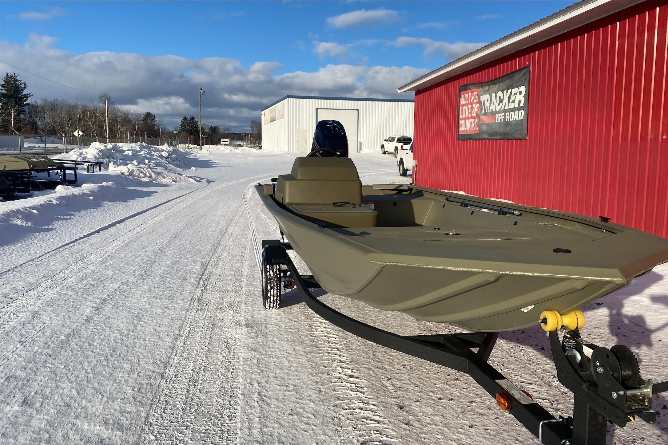 2026 Tracker Grizzly 1648 SC boat on snowy lot near red building.