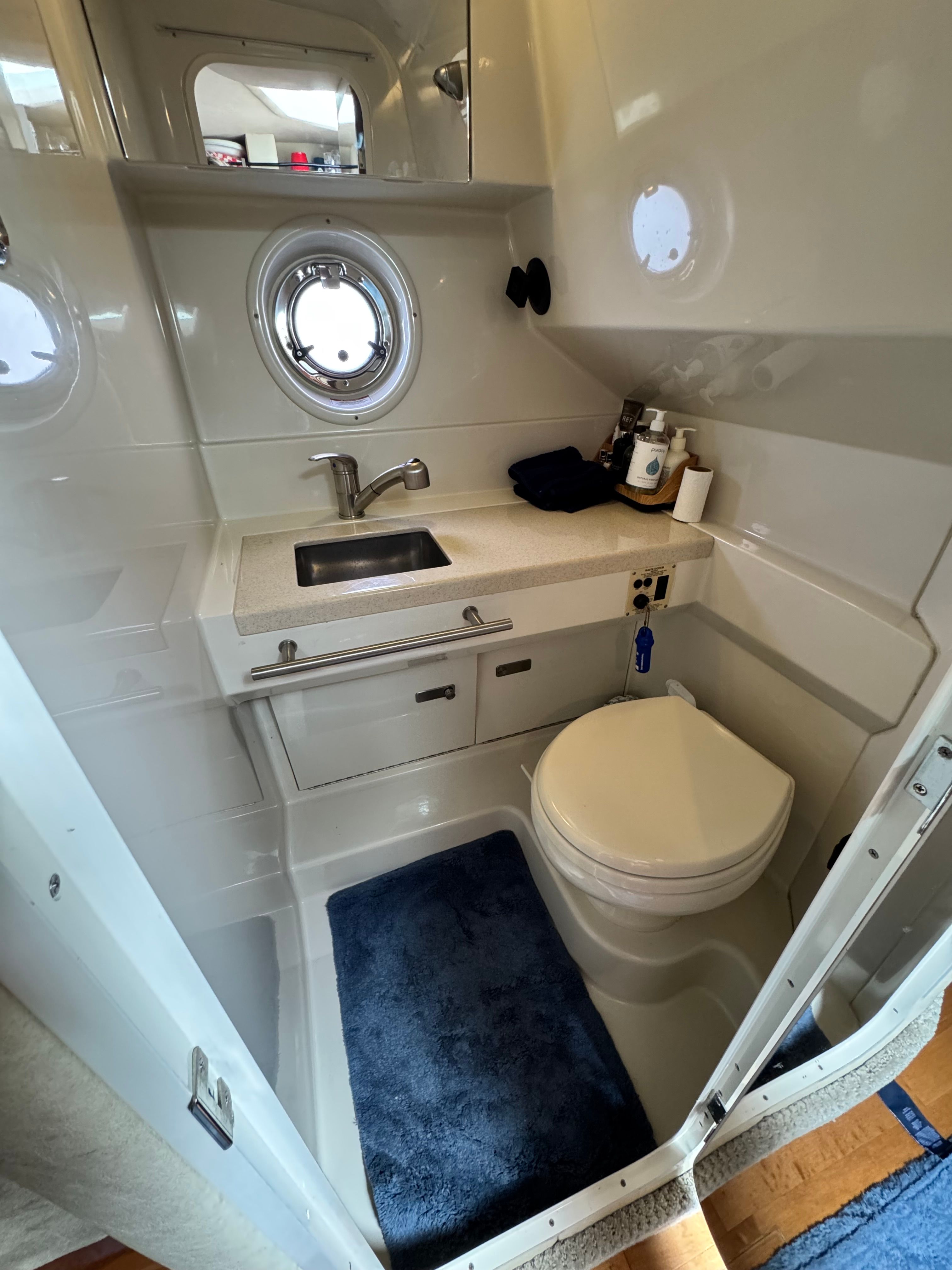 The image shows a boat bathroom with a sink, toilet, and porthole.