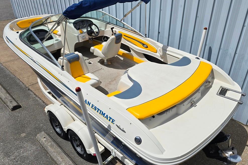 2007 Sea Ray 205 Sport boat with yellow accents, parked on a trailer near a metal building.
