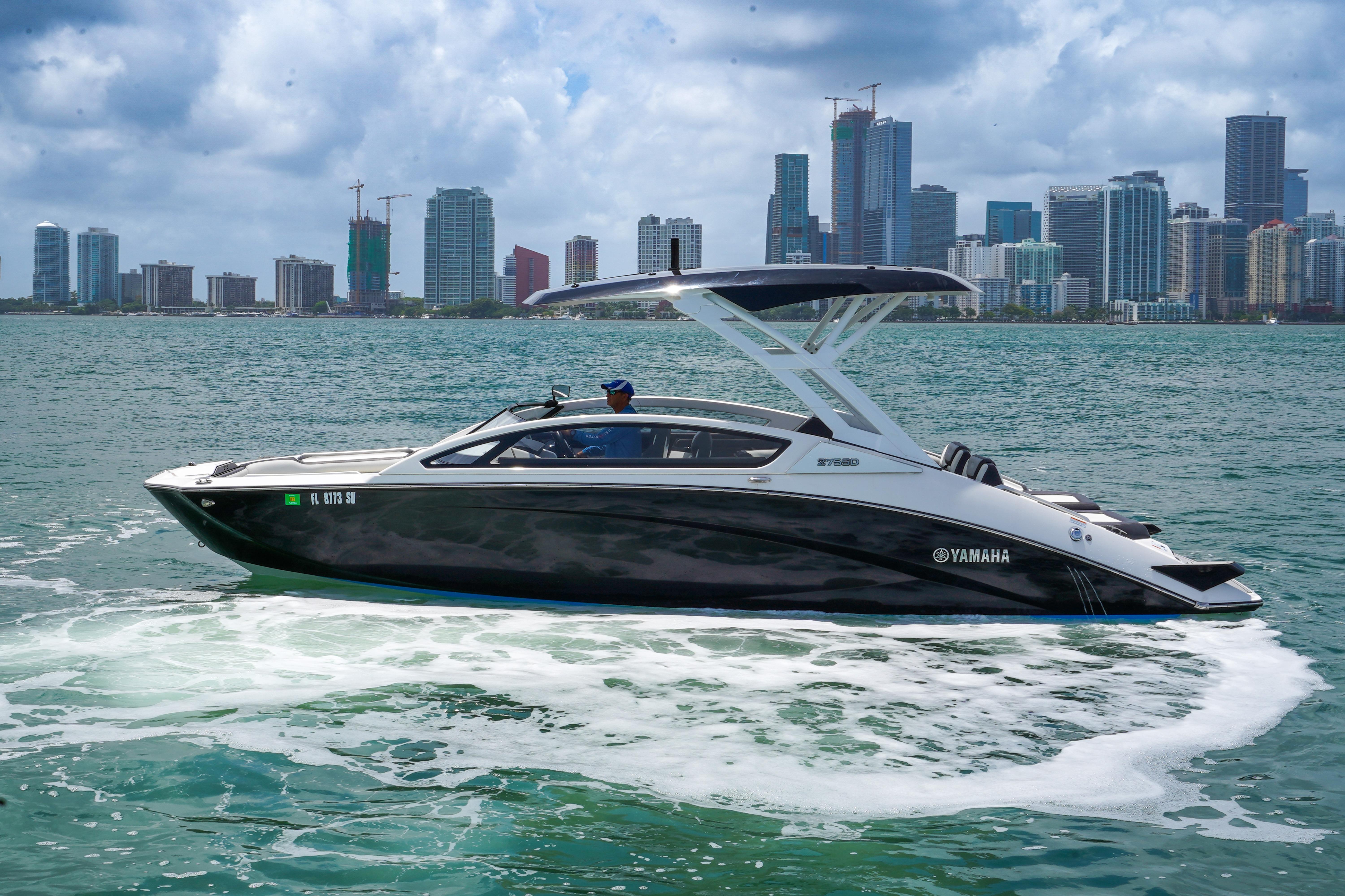 2021 Yamaha Boats 275SD cruising on water with city skyline backdrop.