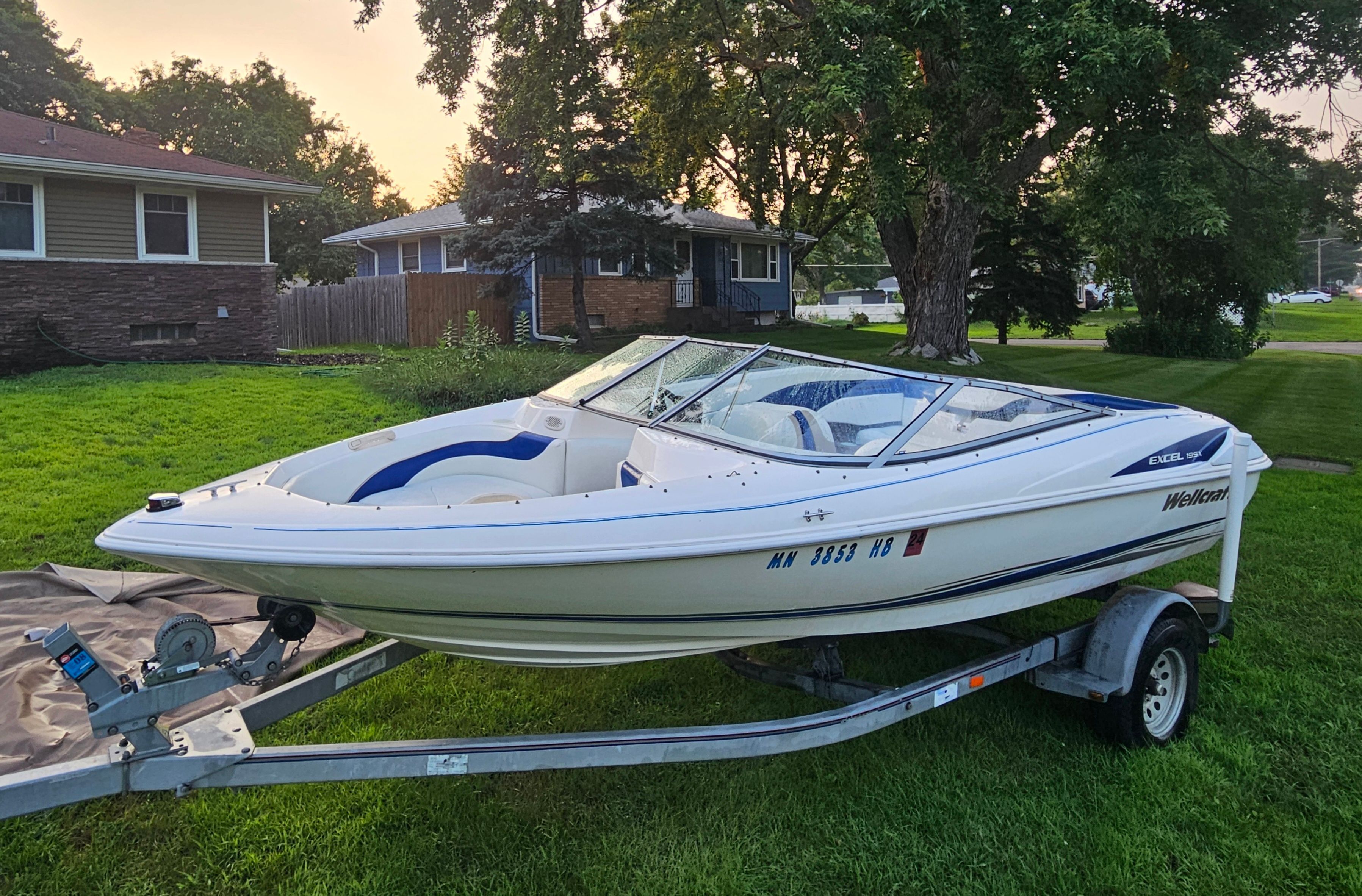 A 1996 Wellcraft Excel boat on a trailer in a grassy yard.
