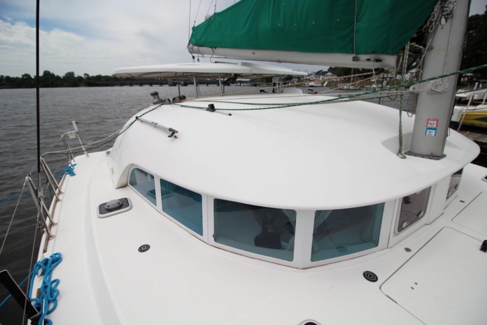 2004 Lagoon 380 catamaran with green sail, docked on a calm river.
