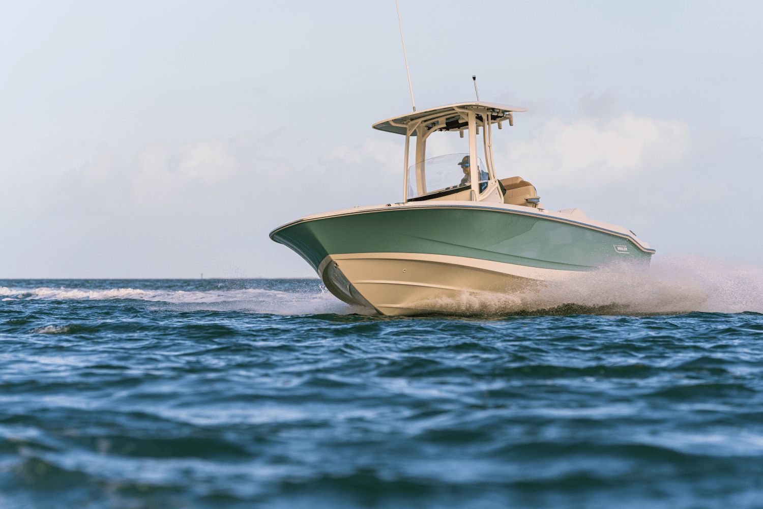 A Boston Whaler 25DA boat speeds across the water, surrounded by blue sky and sea.