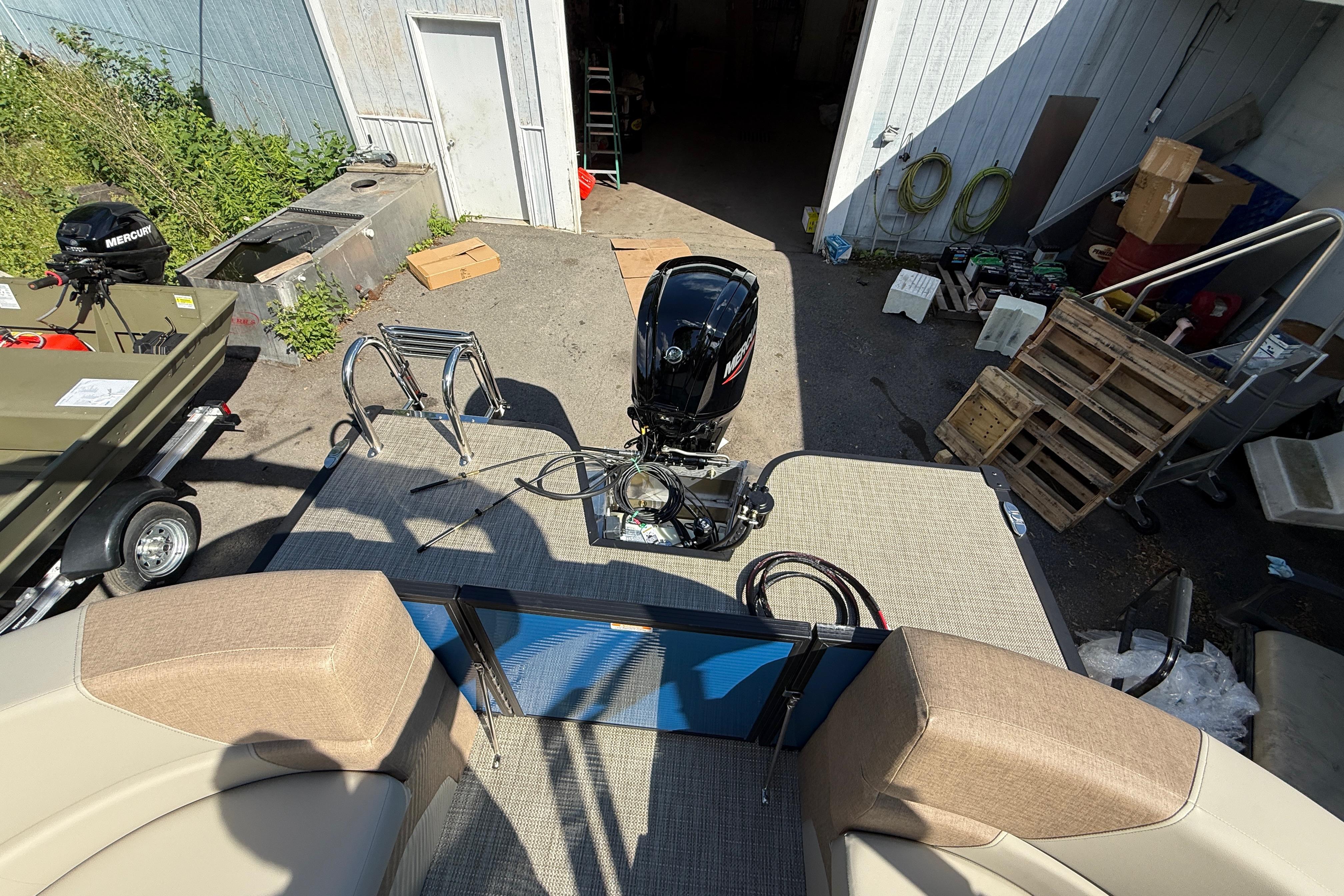 2027 Manitou Aurora RF 23 boat with Mercury outboard motor in a workshop setting.