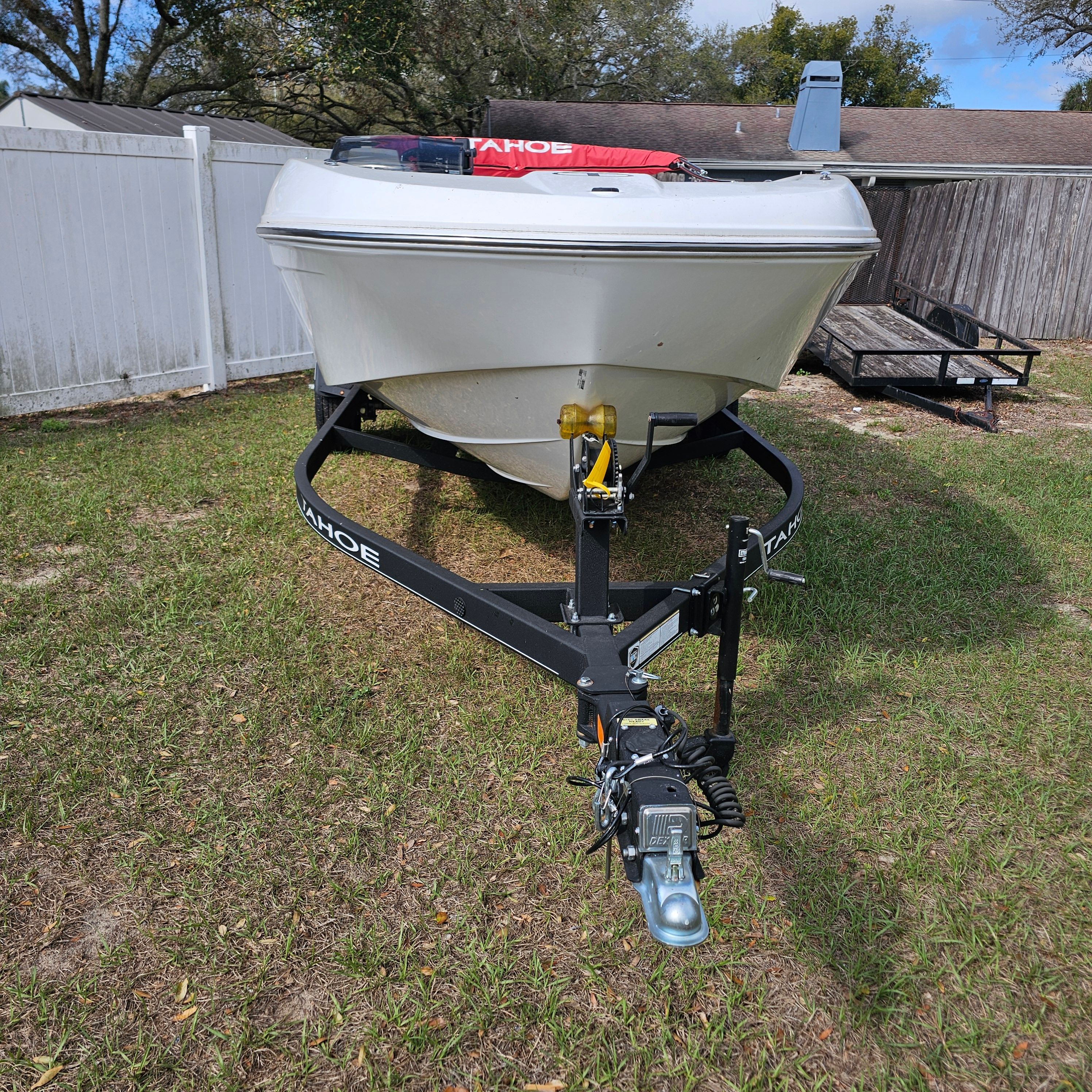 2024 Tahoe T18 boat on trailer, parked on grass near a white fence.