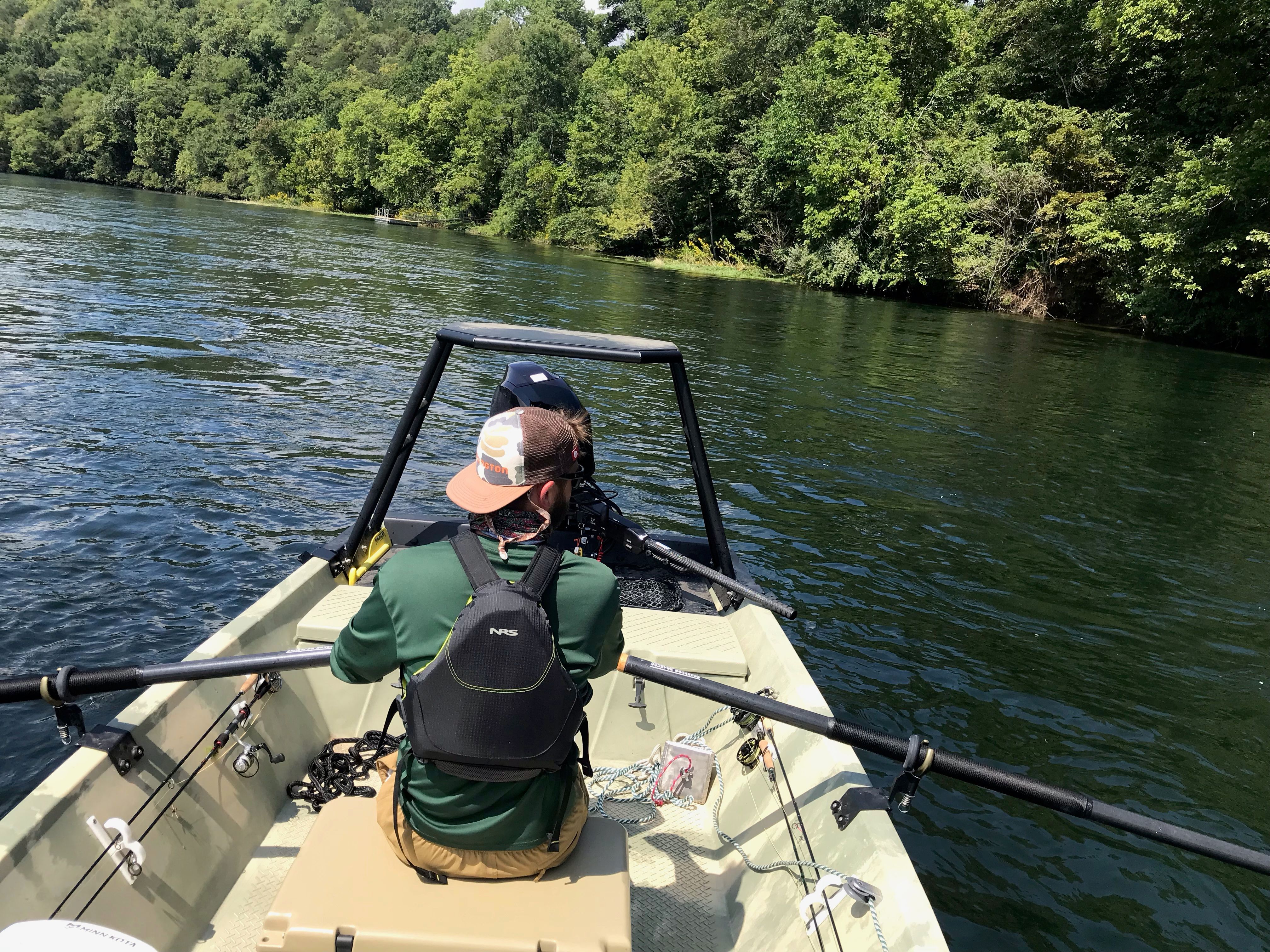 A man rows a boat on a calm river, surrounded by lush greenery.