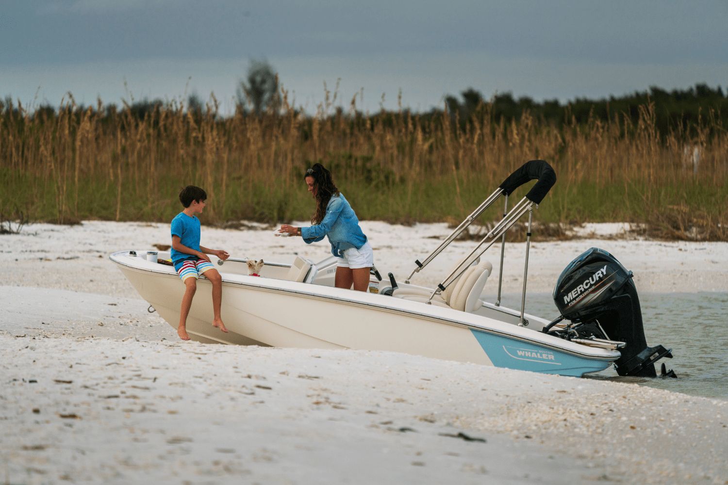A woman and child sit on a Boston Whaler boat at the beach.
