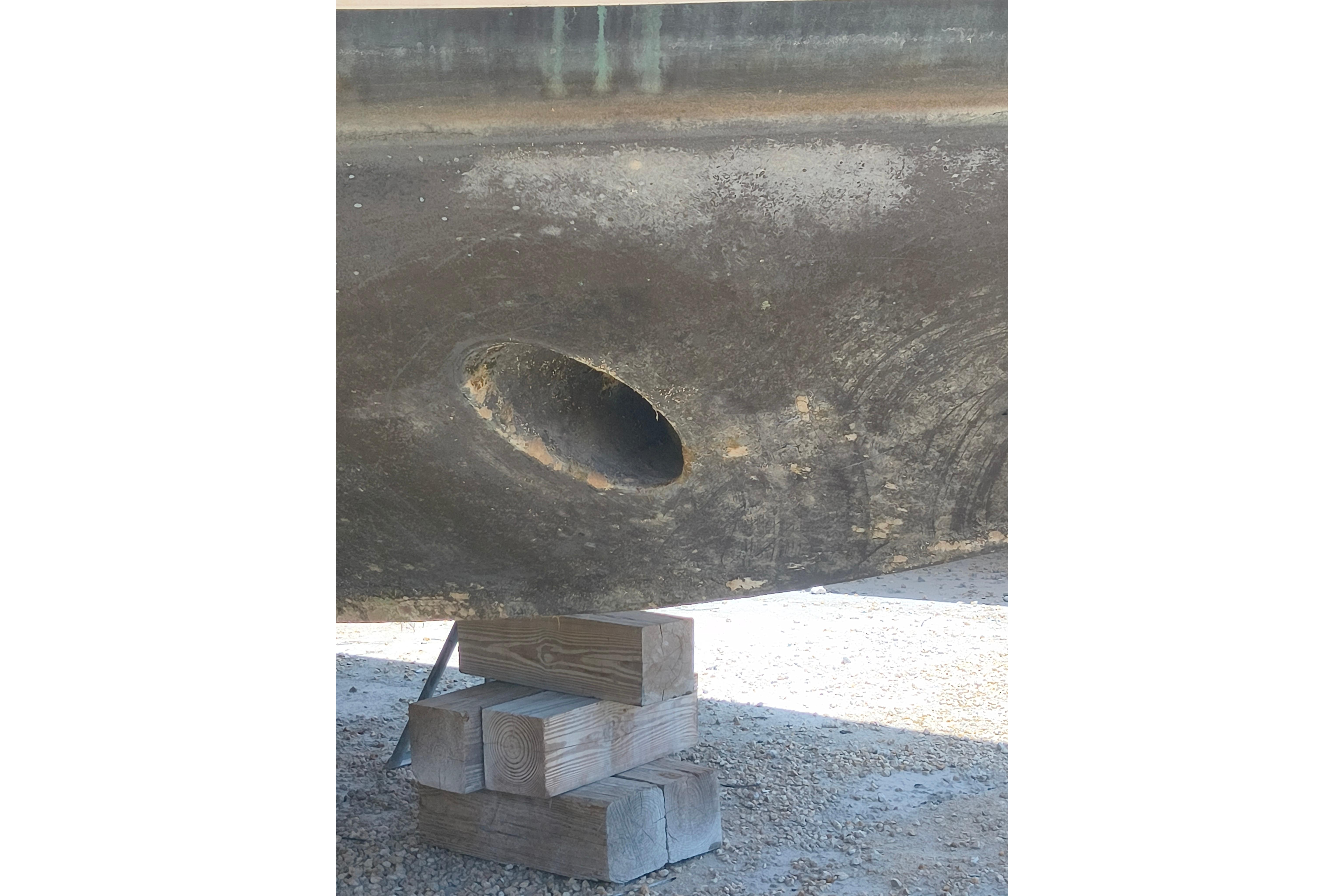 1984 Kadey-Krogen Manatee hull with visible hole, supported by wooden blocks.