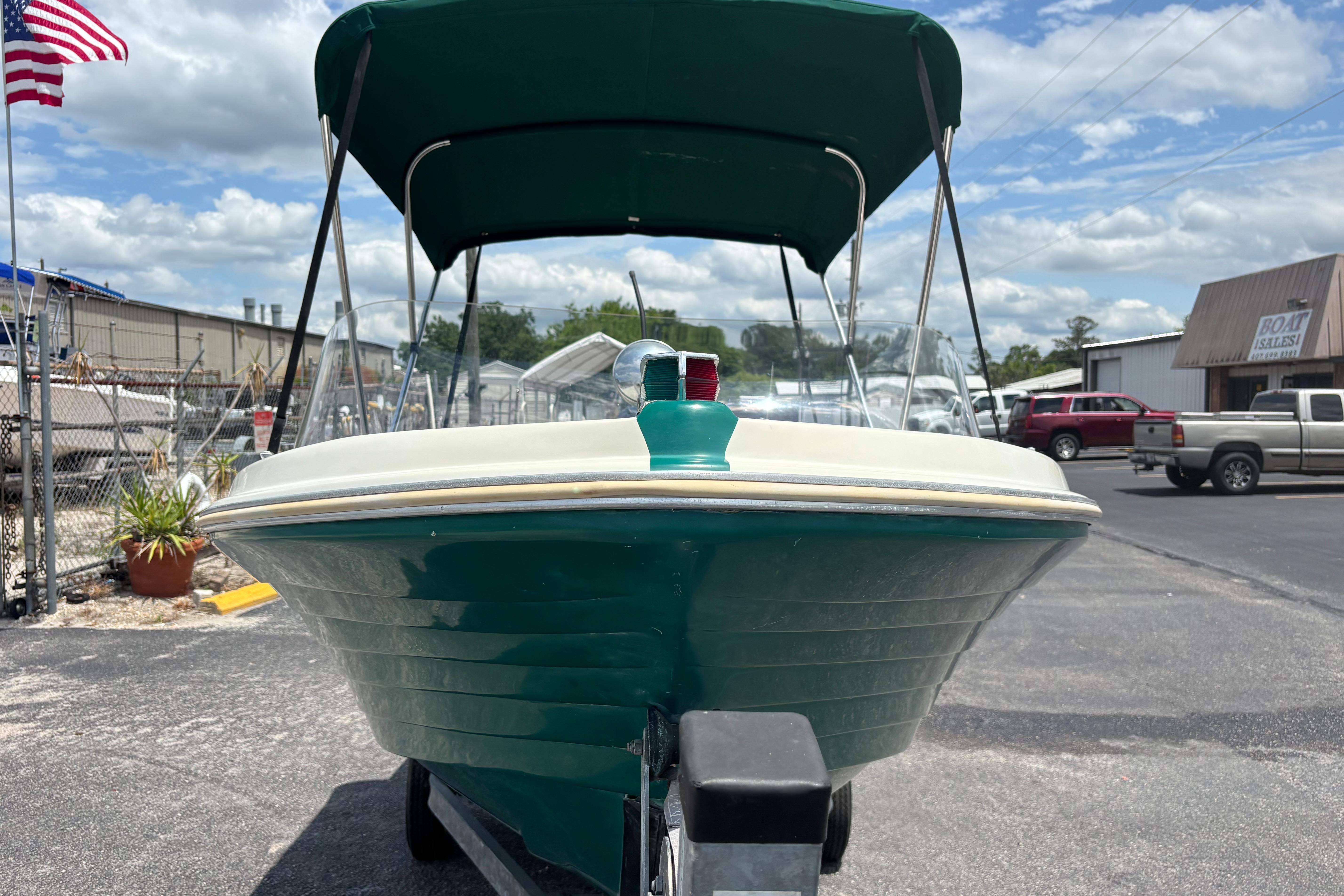 1966 Mohawk 15 boat with green hull and canopy, parked outdoors under a cloudy sky.