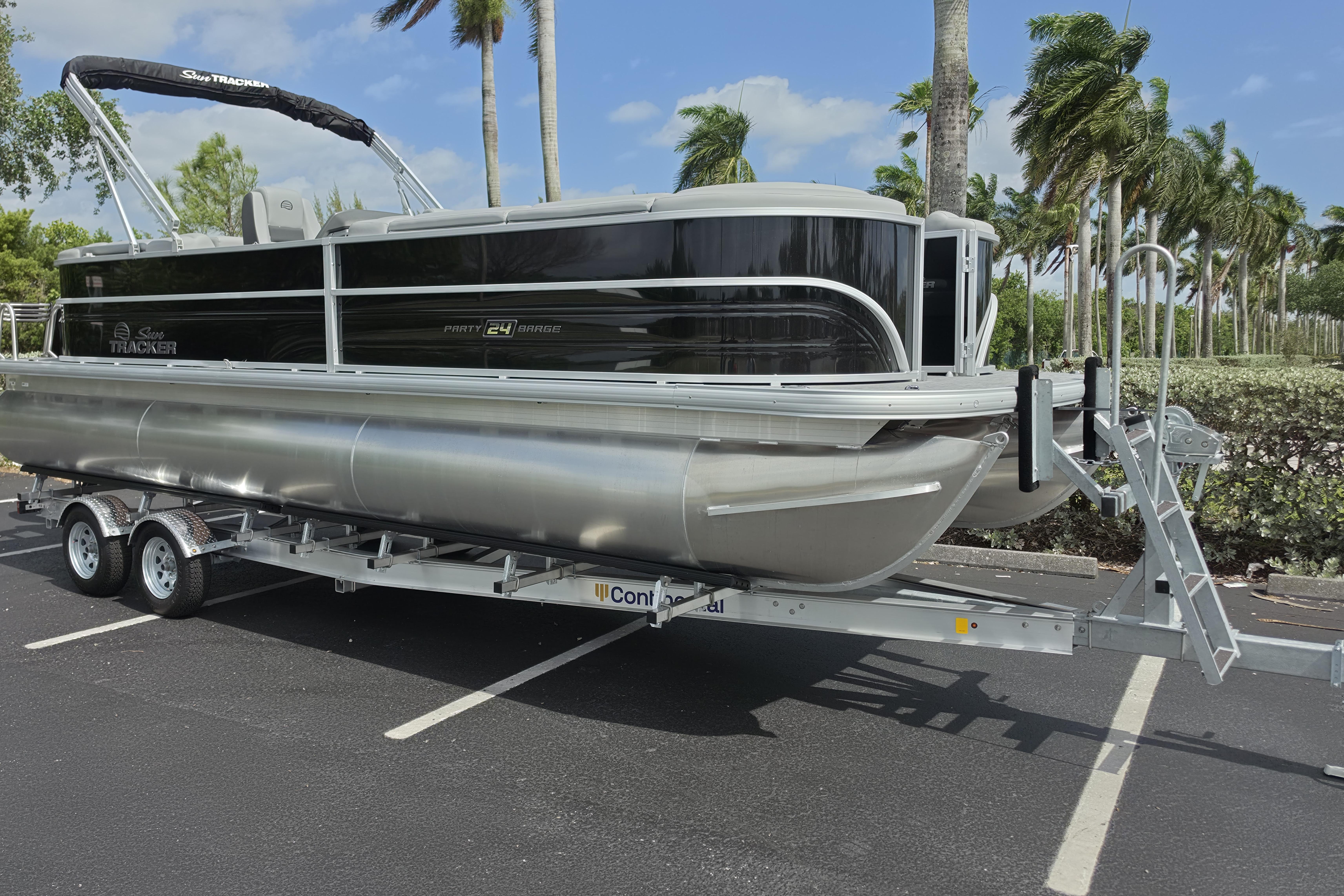 2026 Sun Tracker Party Barge 24 XP3 pontoon boat on trailer, parked under palm trees.