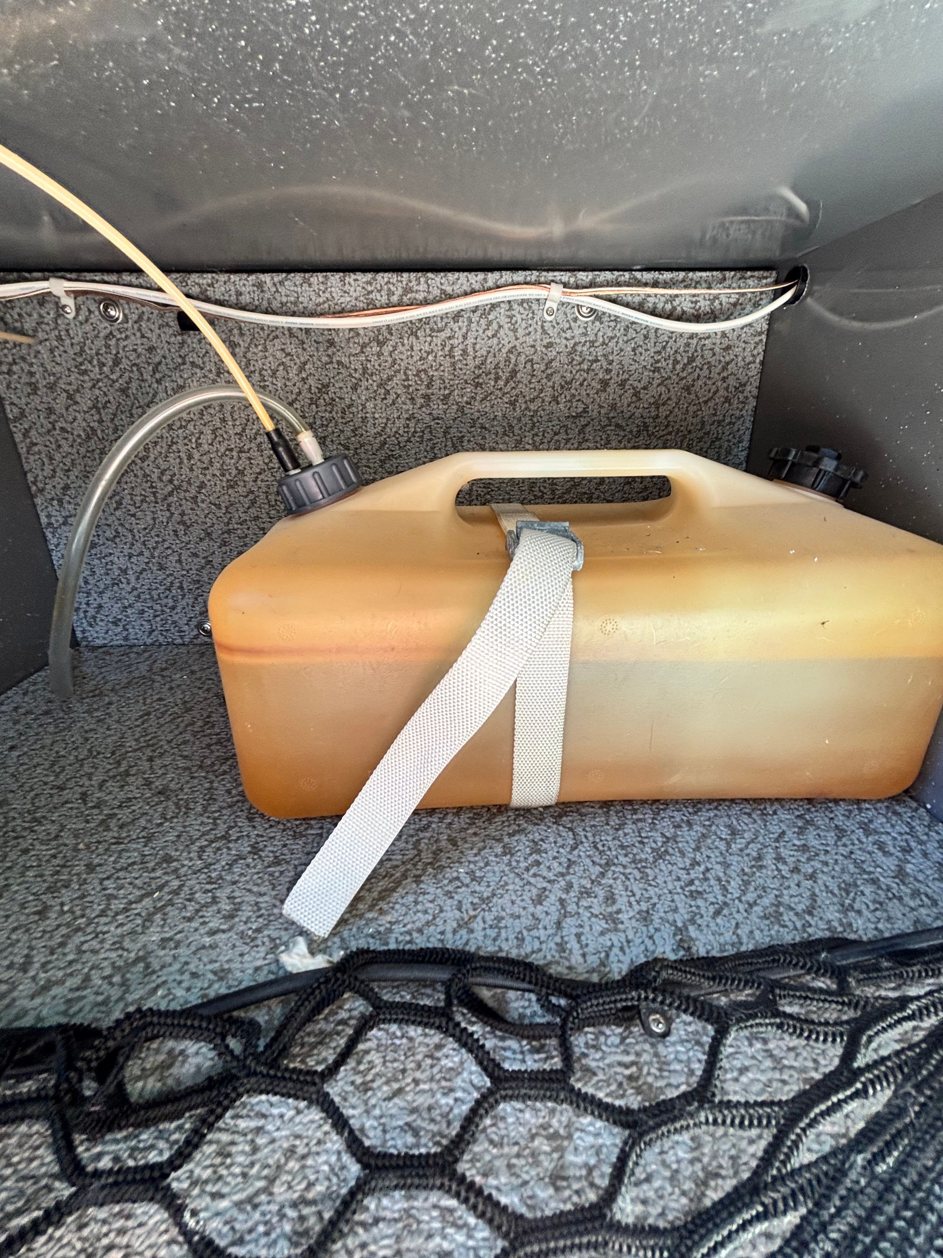 A fuel tank with a carrying strap in a boat storage compartment.
