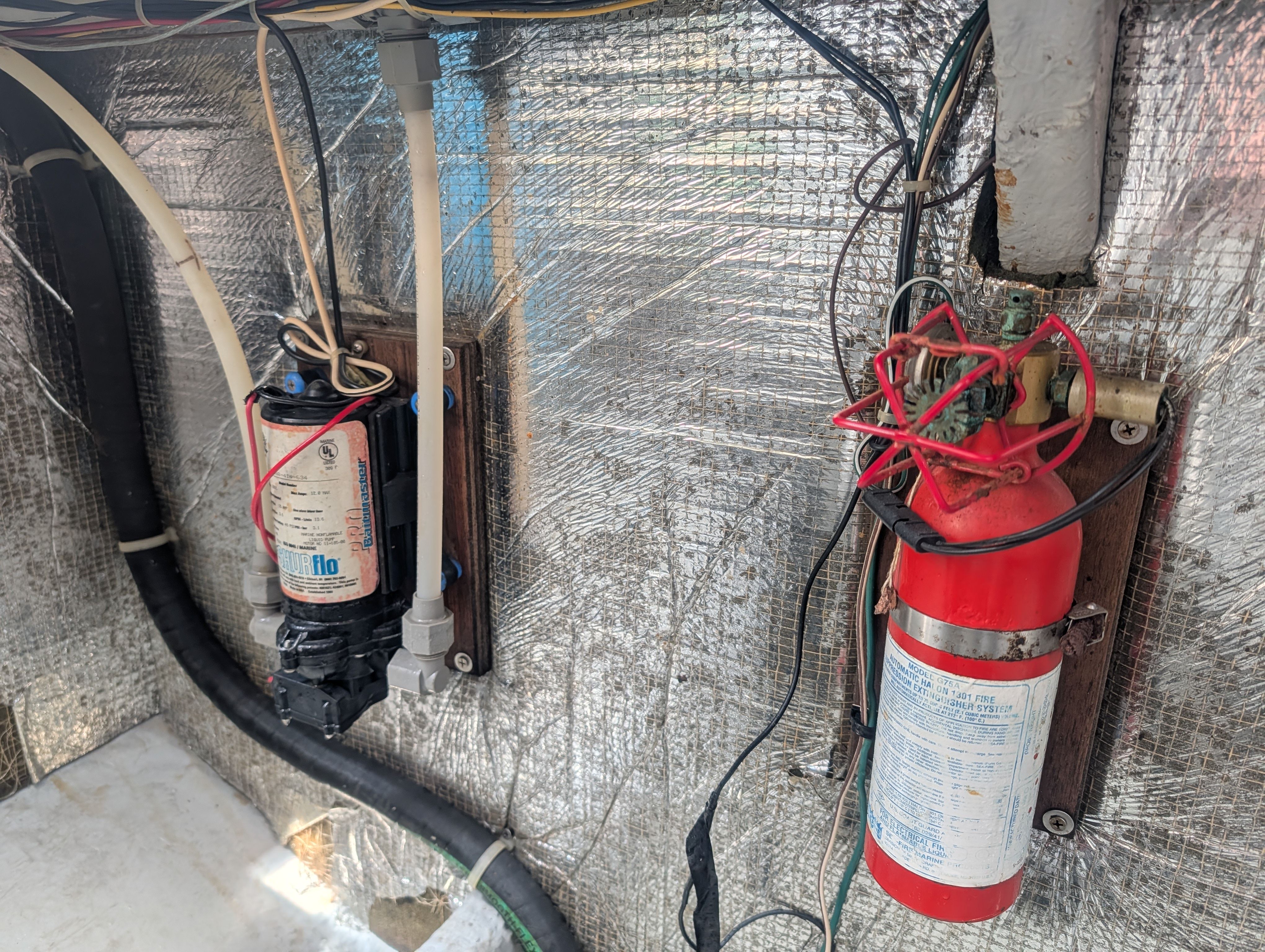 A boat engine room with a fire extinguisher and pump mounted on the wall.