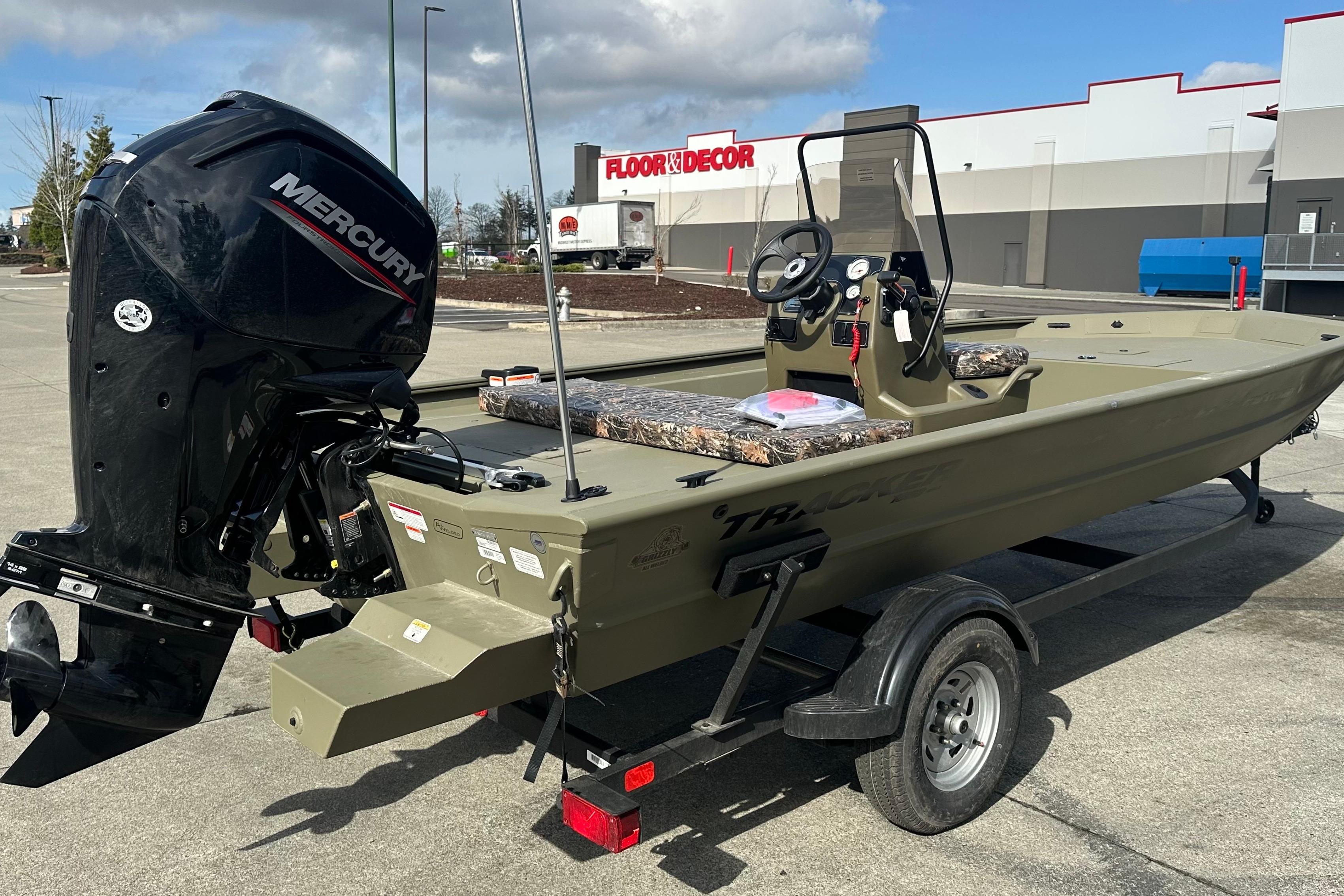 2026 Tracker Grizzly 1860 CC boat with Mercury engine, parked outdoors near a store.
