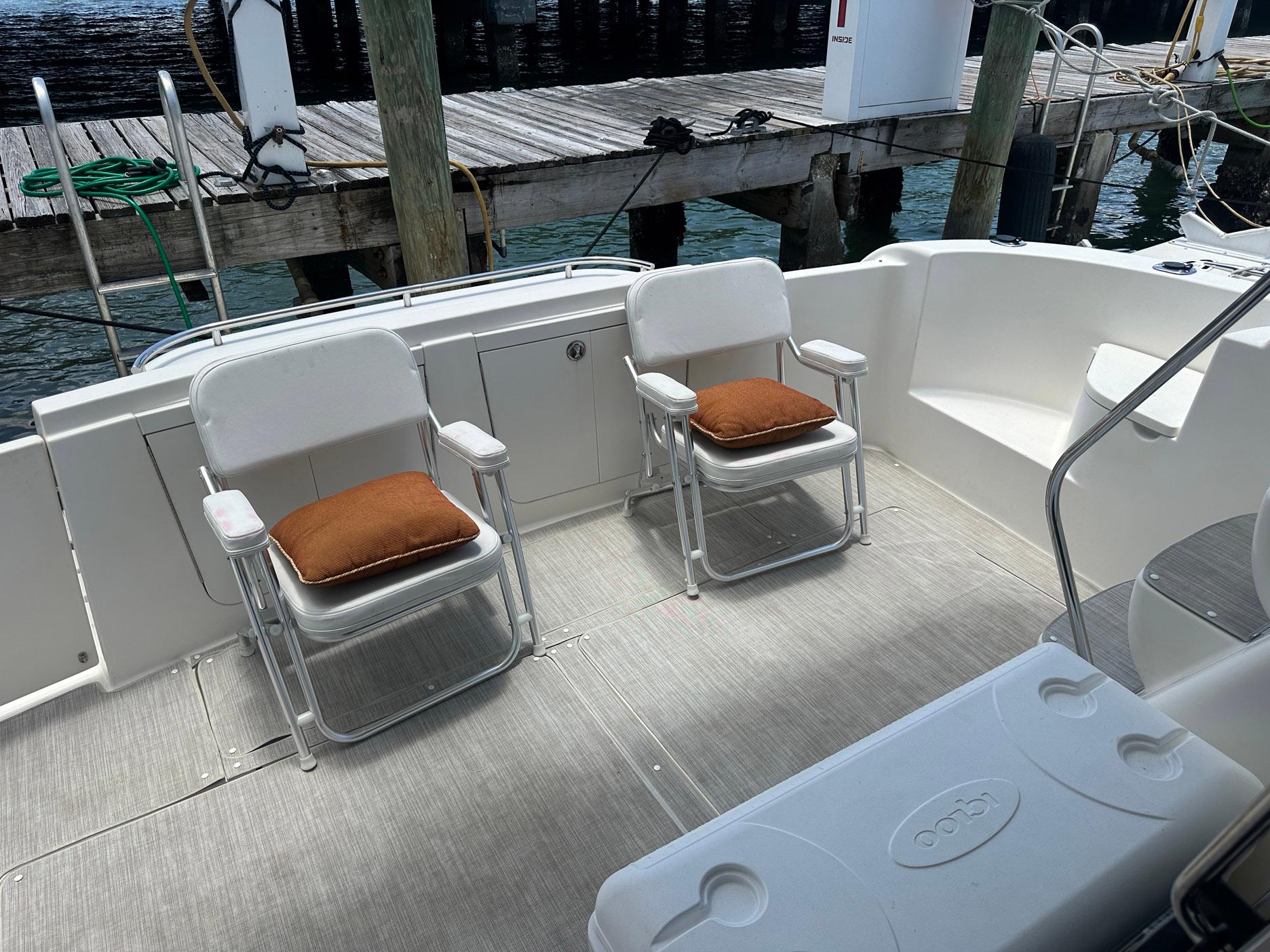2007 Meridian 411 Sedan yacht deck with two chairs and cushions, docked by wooden pier.