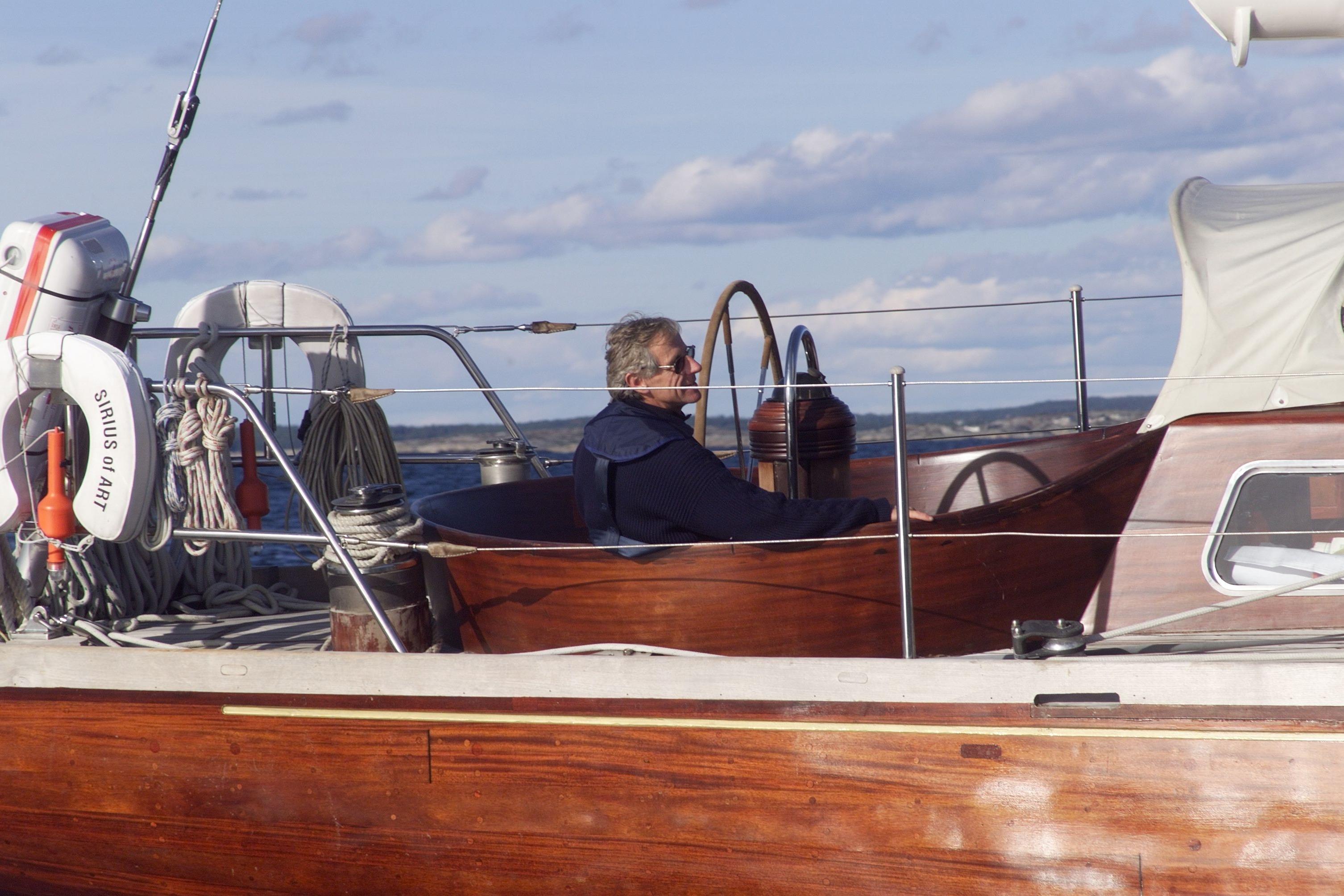 Man steering 1977 Custom Cantiere Valdettaro Le Grazie yacht on calm waters.