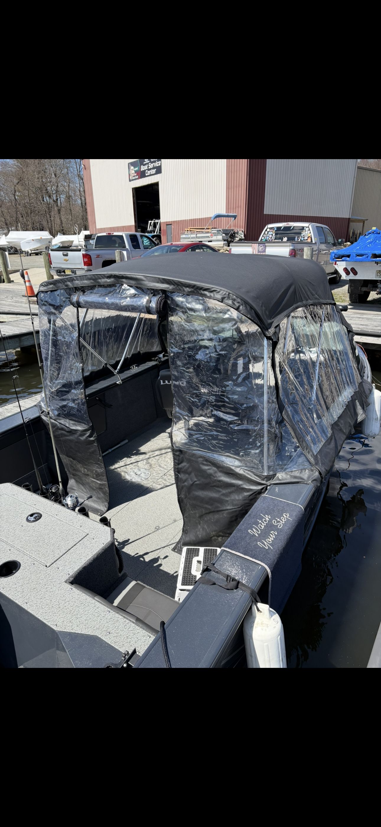 A Lund Fisherman 2075 boat with a canopy and clear side panels, docked at a marina.