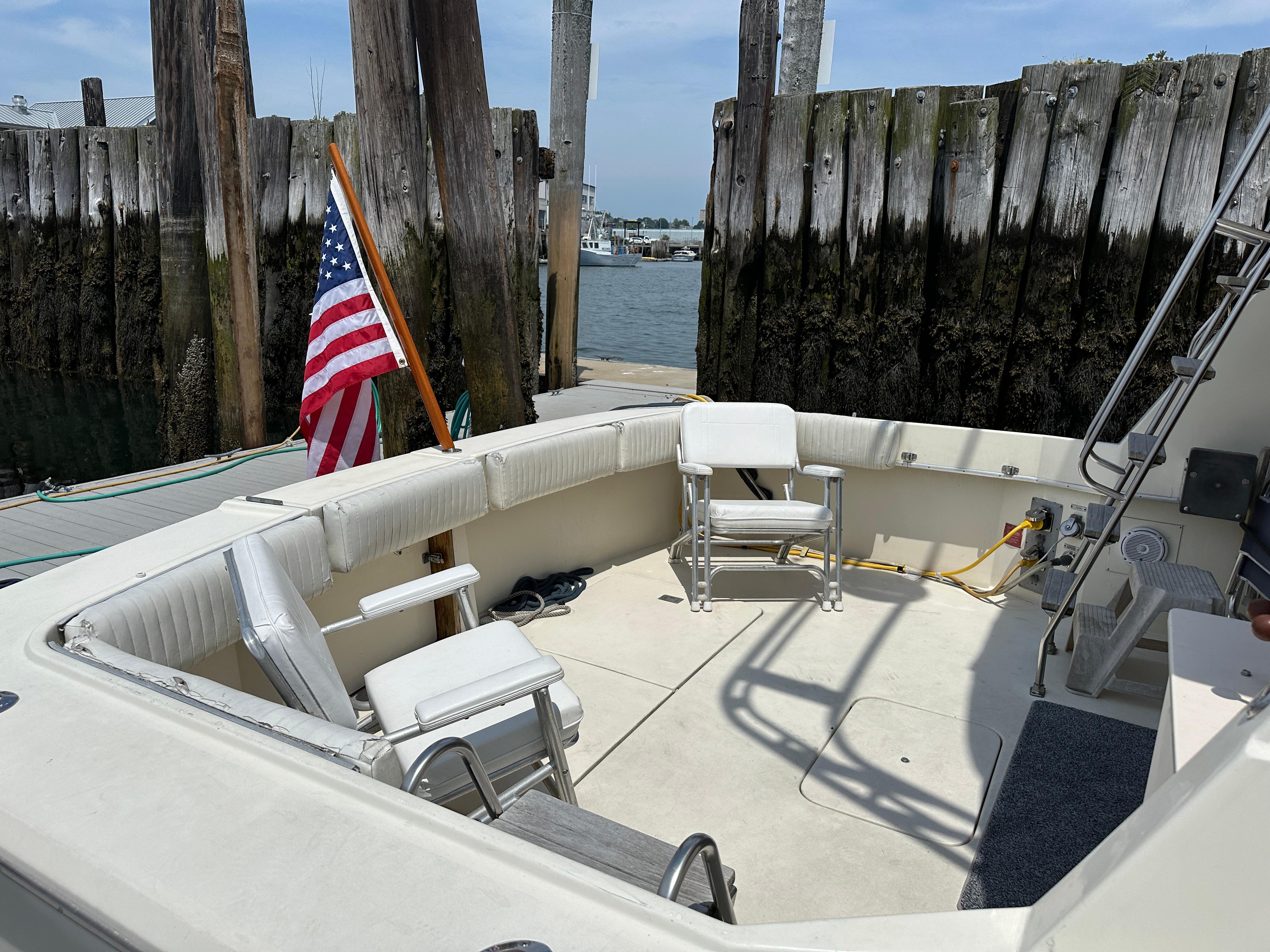 1985 Hatteras 36 Convertible boat with seating area and American flag at dock.