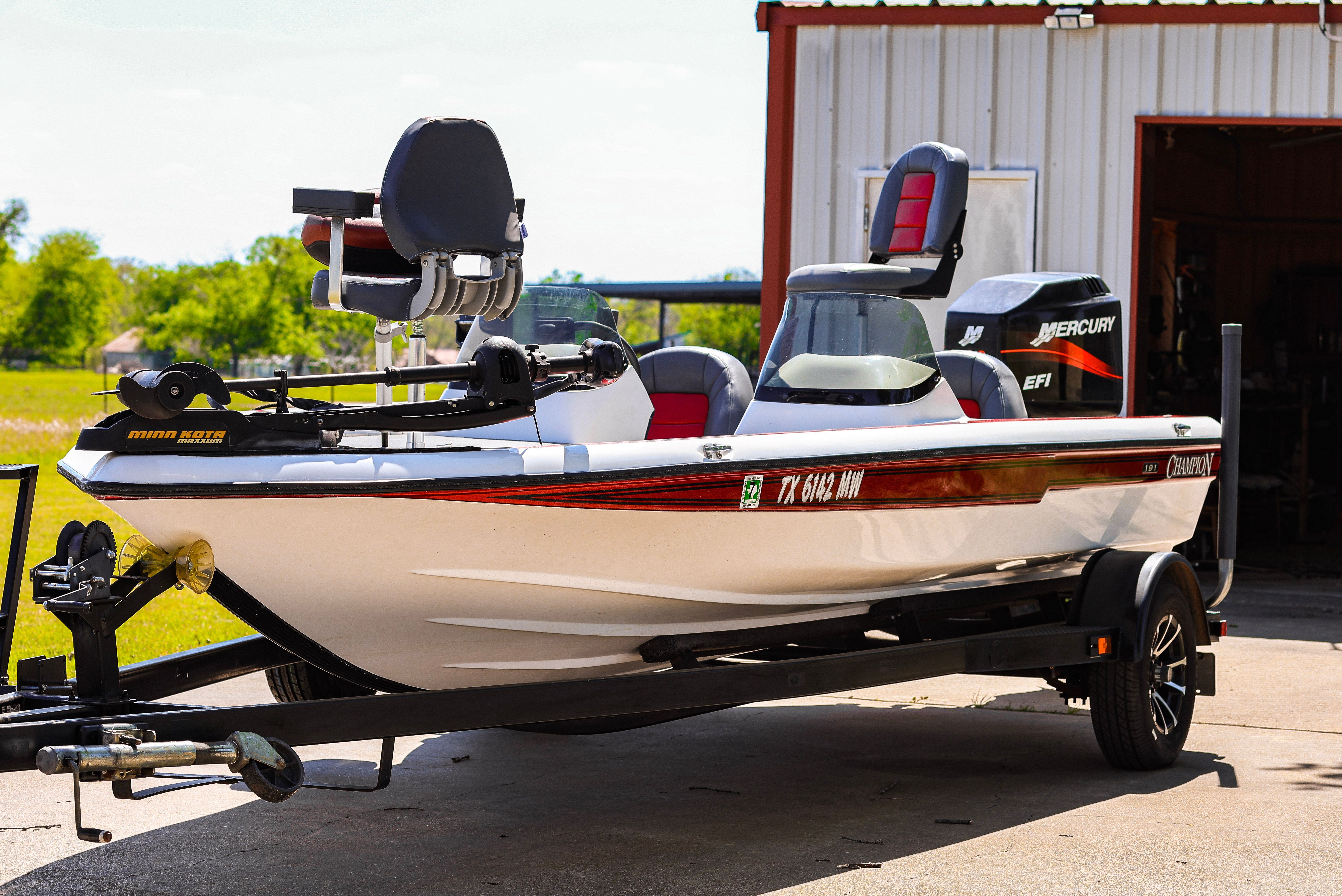 A white 1999 Champion bass boat on a trailer in front of a garage.
