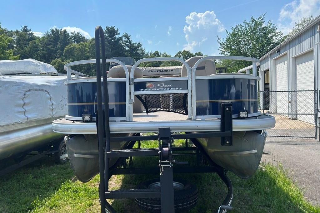 2023 Sun Tracker Bass Buggy 18 DLX pontoon boat parked outdoors near a storage facility.
