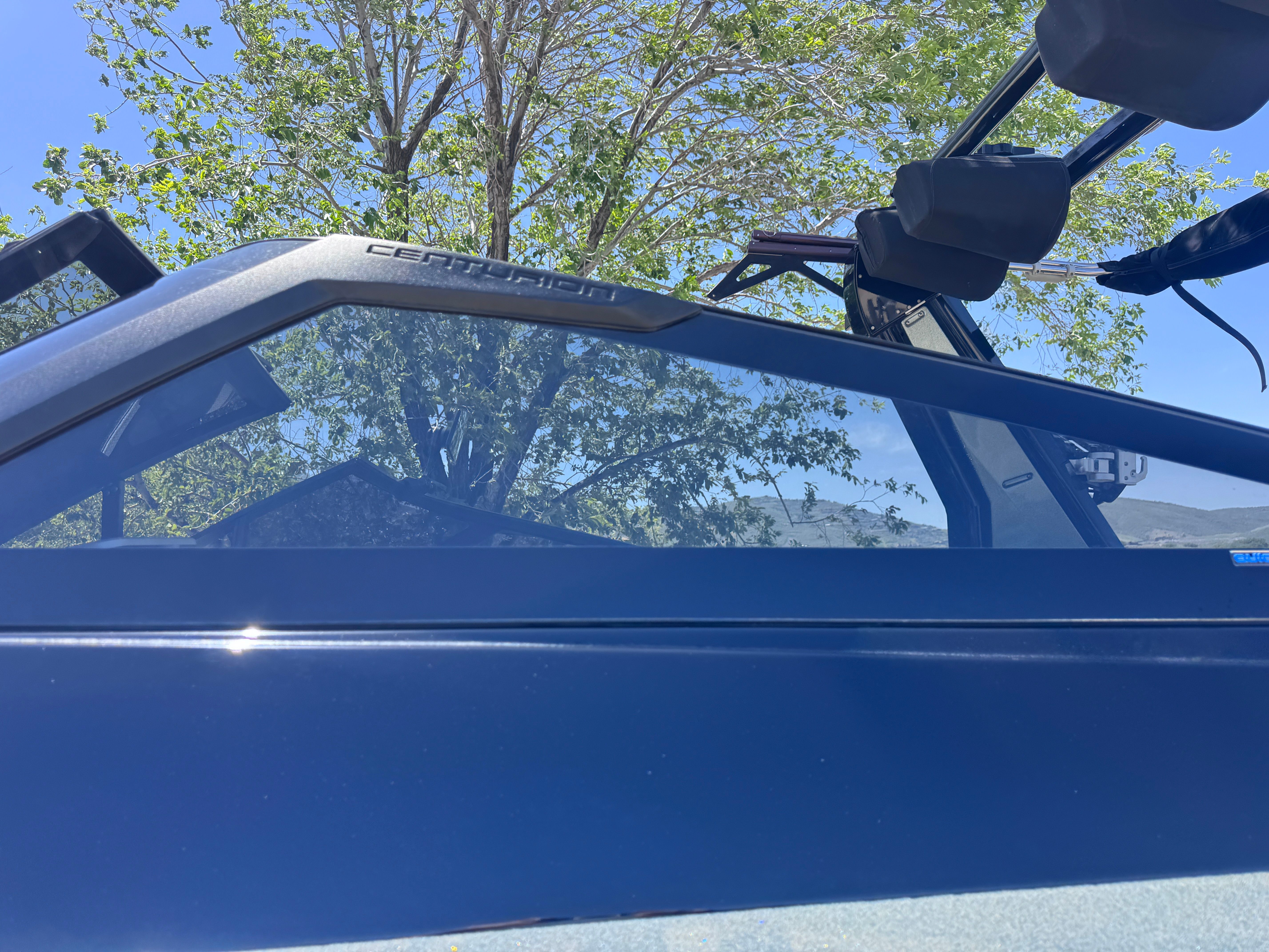 A 2022 Centurion Ri230 boat with a blue hull and tinted windows, parked in front of a tree.